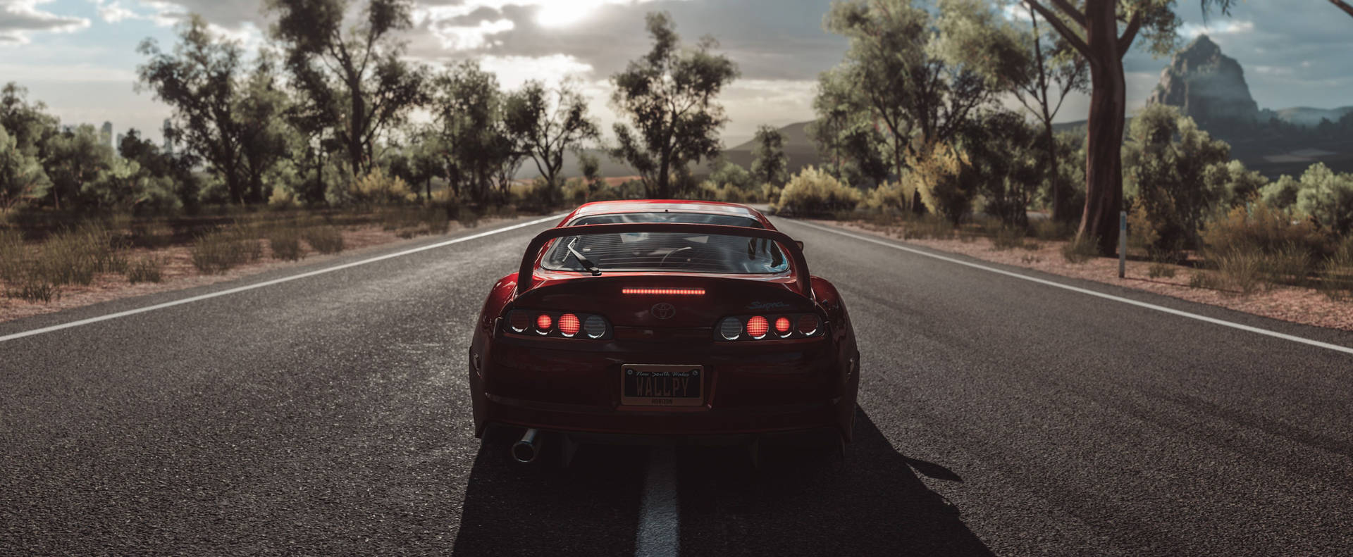 紅色跑車在日落時分行駛在鄉村道路上，穿過森林景觀。 — Toyota Supra 壁紙