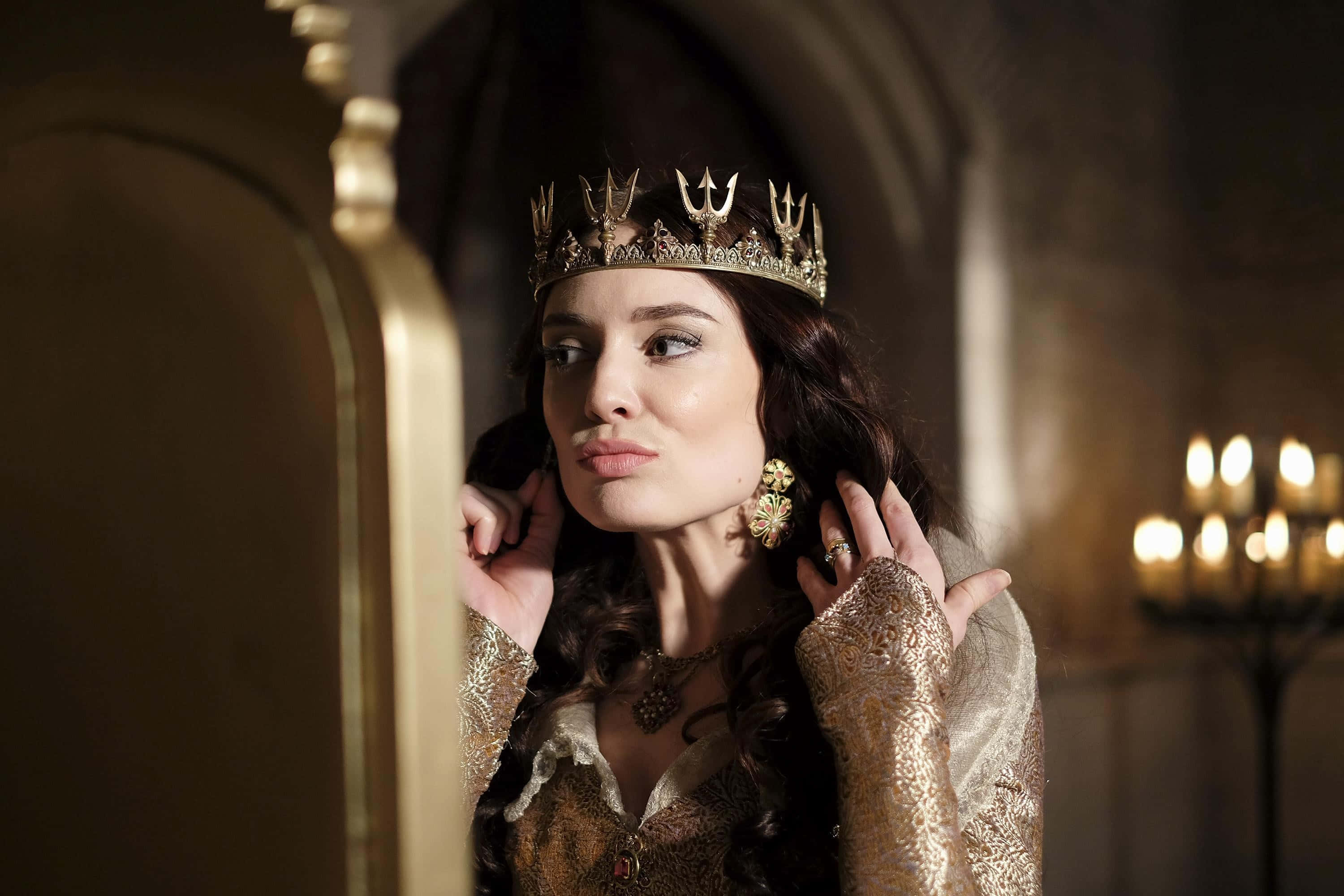 Mallory Jansen 桌布 壁紙 — 一位高貴的女性戴著華麗的金色王冠和長袍，在燭光映照的中世紀房間裡若有所思地凝視著鏡子。