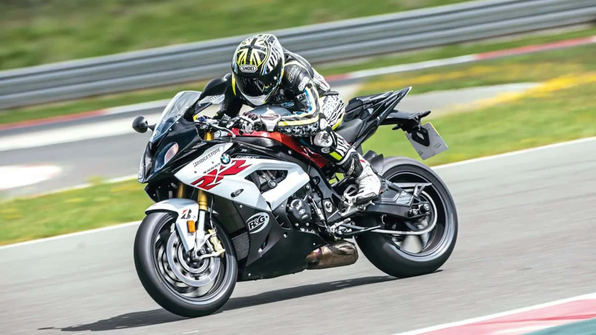  壁紙 — 一名騎士在陽光普照的賽道上，騎著白色和黑色的BMW S1000RR機車，傾斜入彎，背景有模糊的綠色草地和護欄。