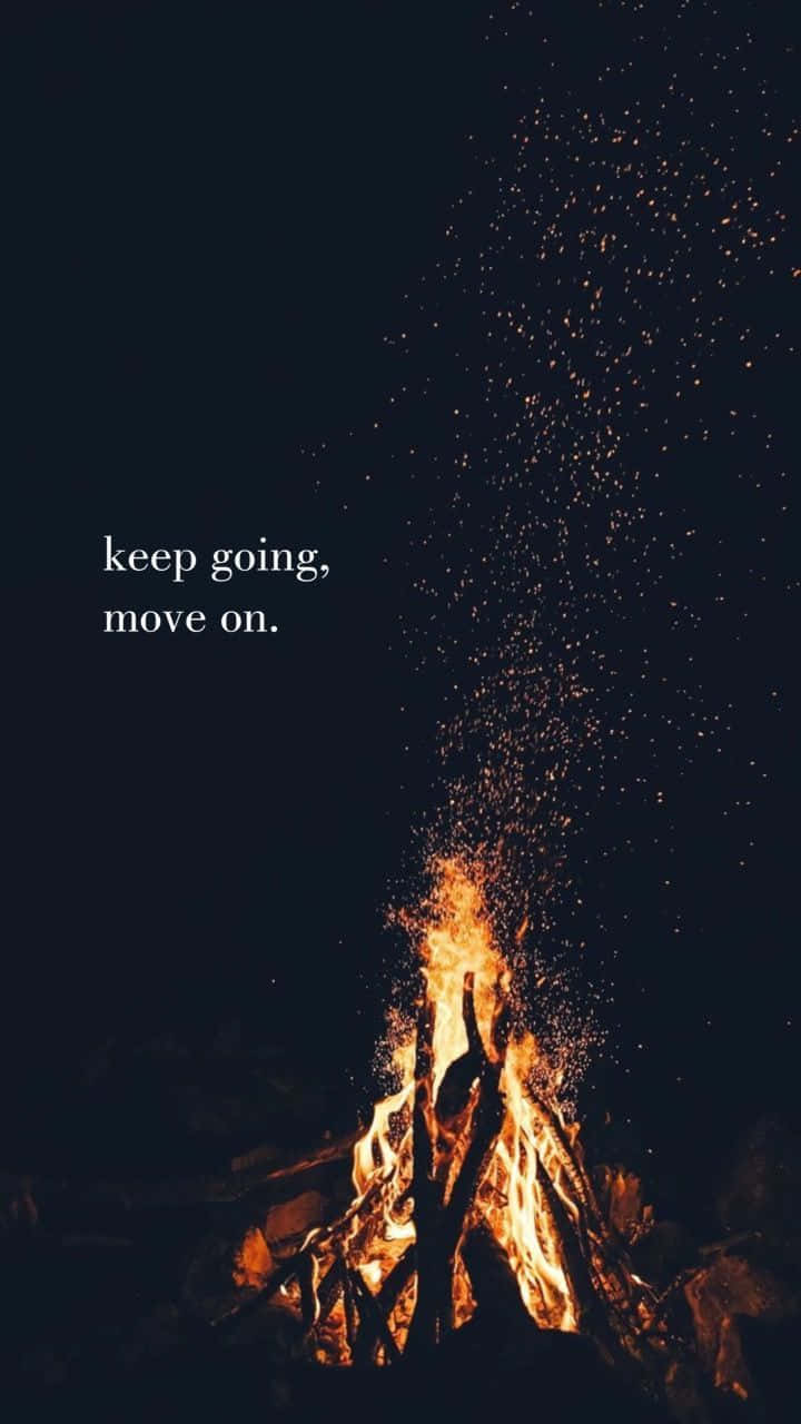  壁紙 — 夜晚的營火咆哮著，火花向上飛向黑暗的天空，上面有文字 keep going move on。