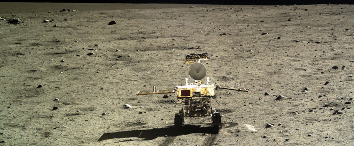 Lunar Rover 桌布 壁紙 — 一個帶有碟形天線的機器人探測車站在荒蕪的灰色月球表面，點綴著岩石，在明亮的陽光下。