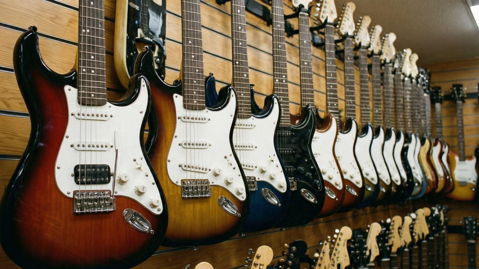 Guitar Wall Display 壁紙 — 一排各種顏色的電吉他整齊地掛在音樂店的木牆上。