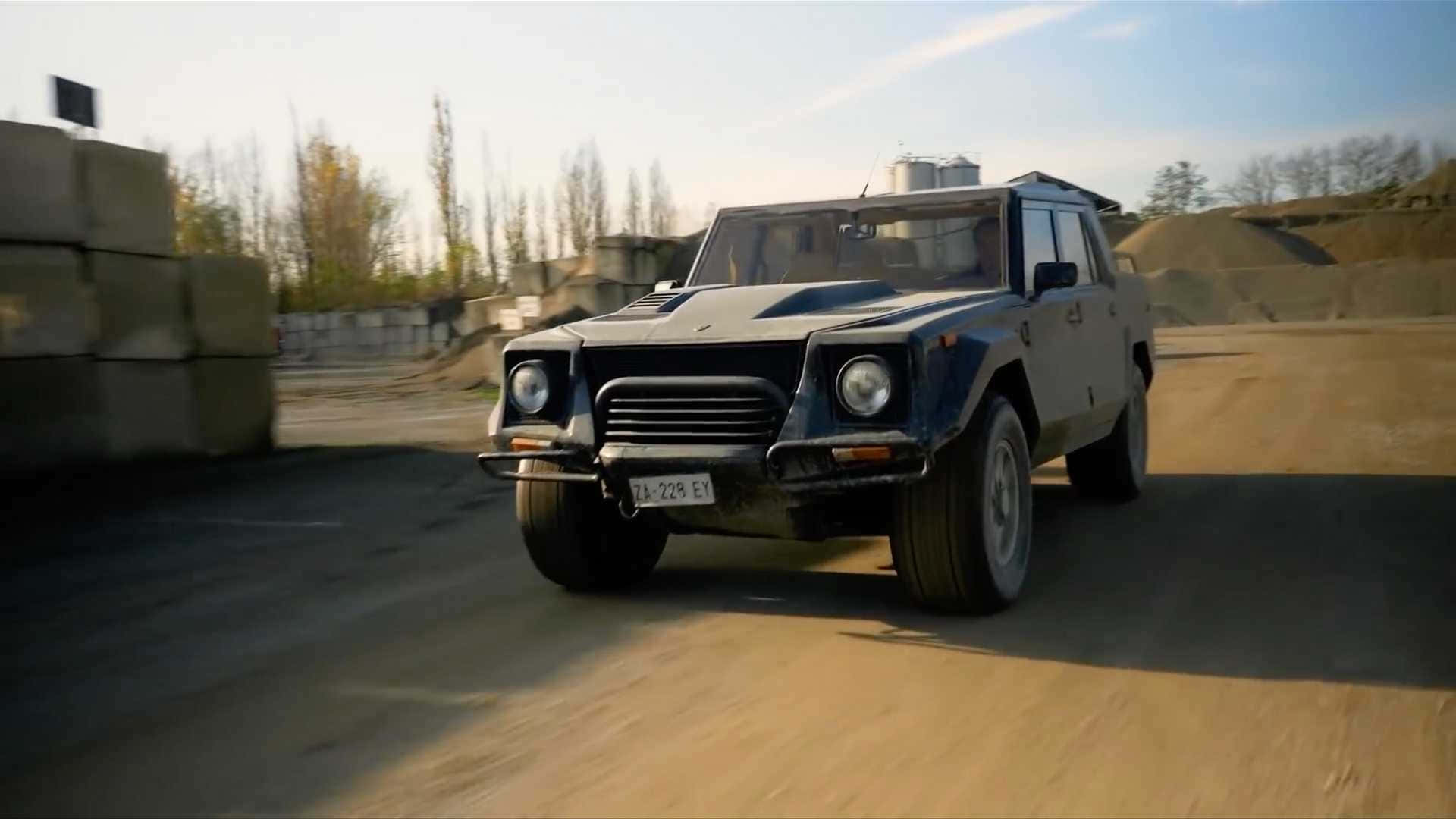 Lamborghini Lm002 桌布 壁紙 — 一輛堅固的藍色藍寶堅尼LM002在晴朗的天空下行駛在一條塵土飛揚的道路上，經過堆疊的混凝土塊。
