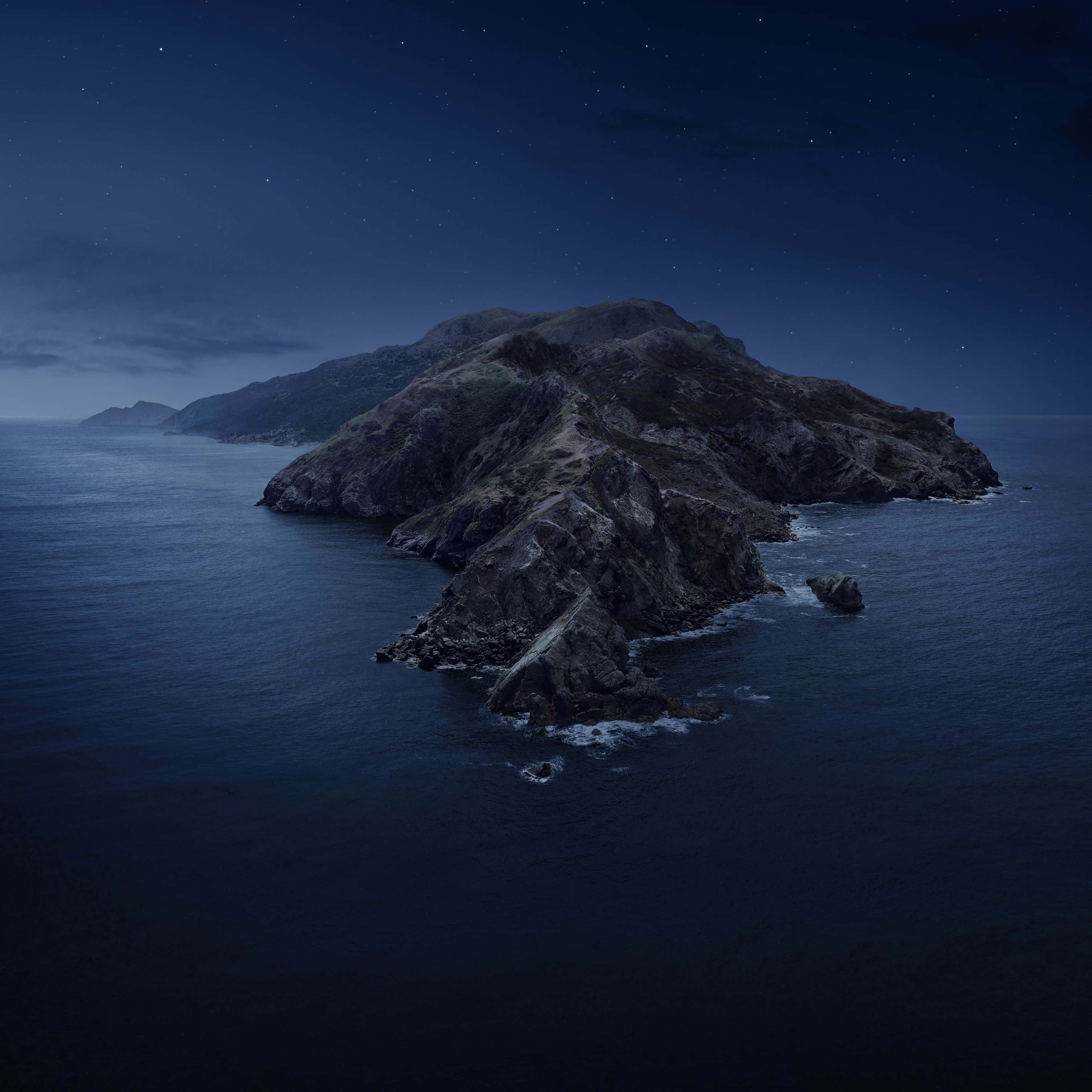 Night Mode 桌布 壁紙 — 一座崎嶇的岩石島嶼從深藍色的海洋中升起，在繁星點點的夜空下，有散落的雲朵。