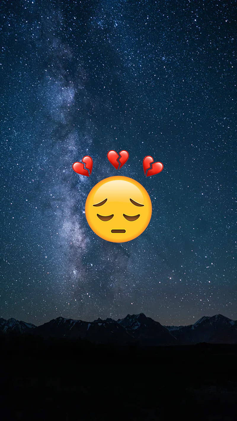 悲傷表情符號帶有破碎心心，襯托著星空夜空和山脈輪廓。 — 夜空 壁紙