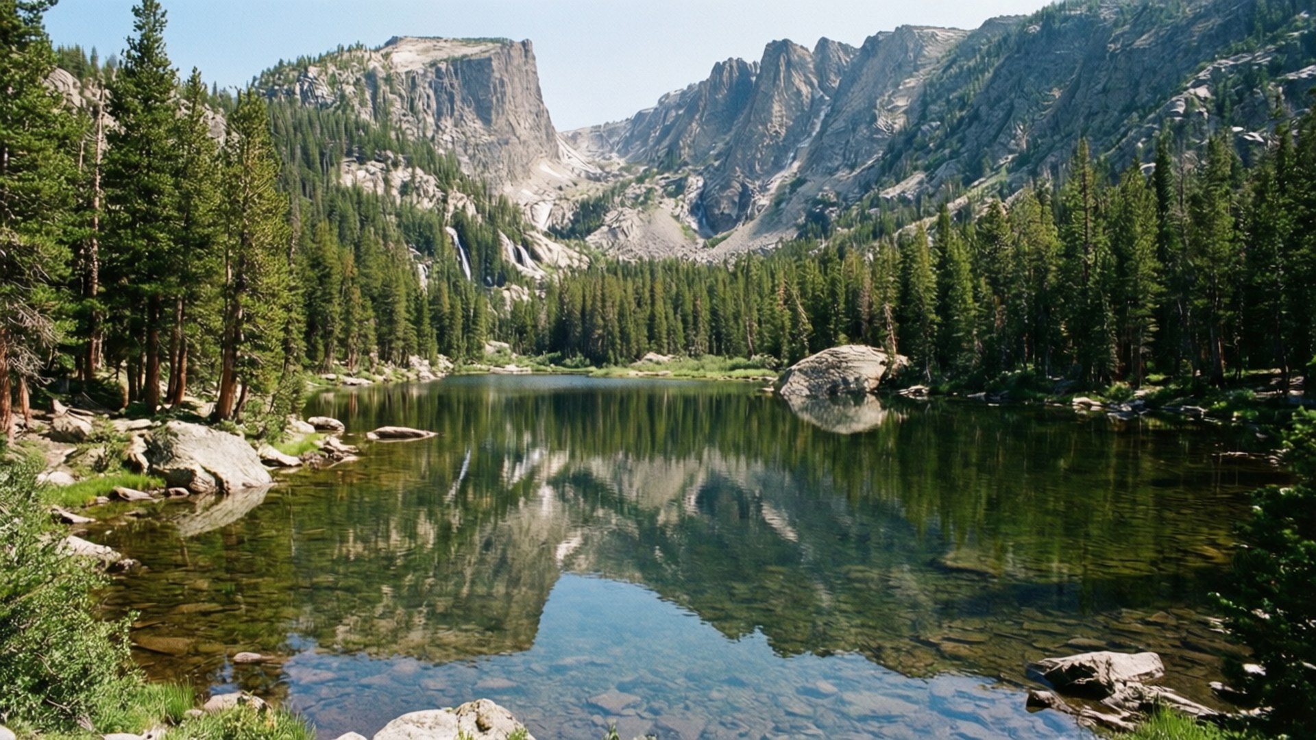 Yellowstone Lake Reflections 壁紙 — 寧靜的高山湖泊映照出高聳的花崗岩懸崖和茂密的松樹林，在清澈的藍天下。