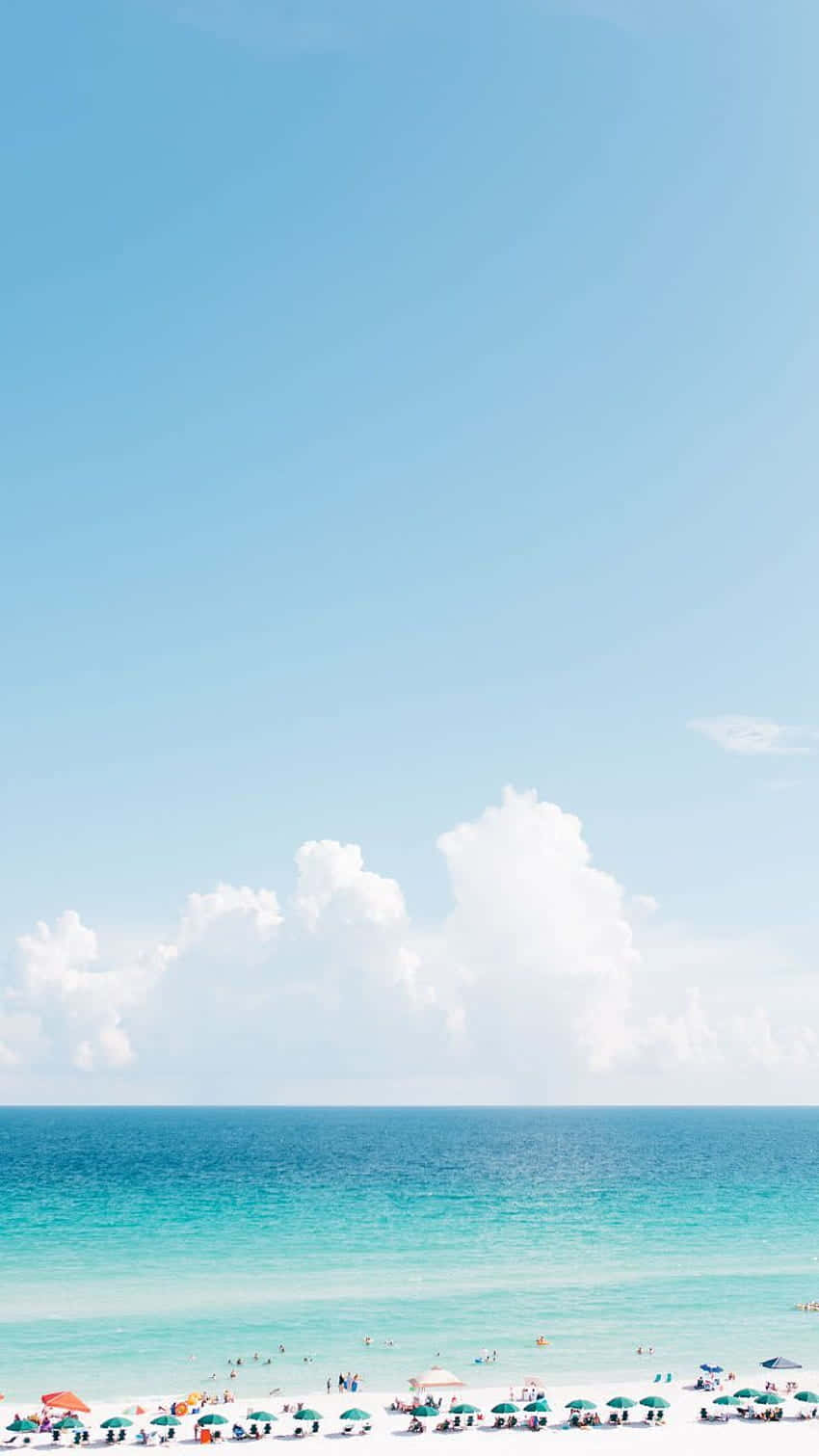  壁紙 — 寧靜的海灘場景，有碧綠的海水、白色的沙灘和散落的沙灘傘，在廣闊的藍天下有蓬鬆的雲朵。