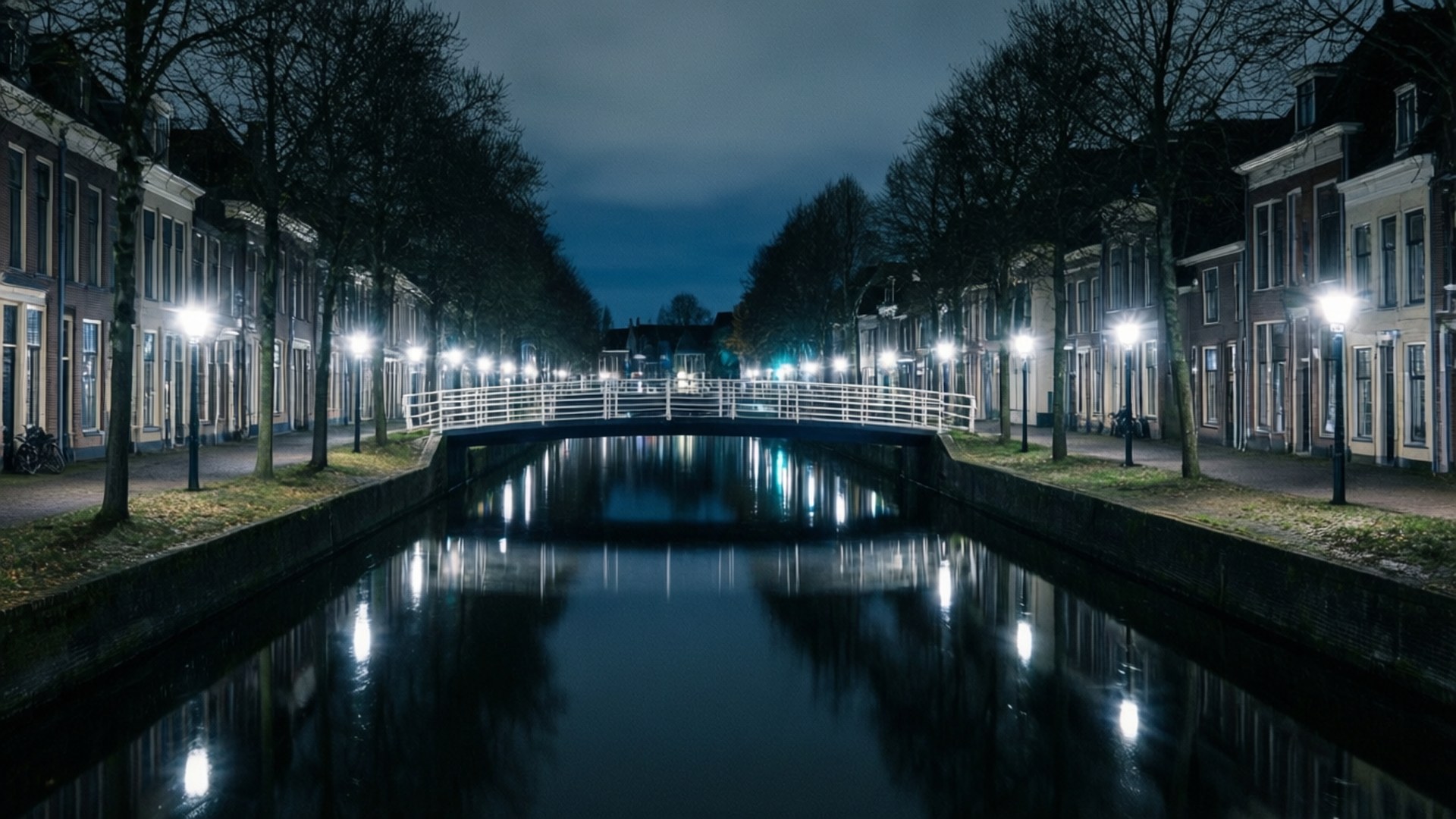 Apeldoorn 桌布 壁紙 — 一條寧靜的夜晚運河，兩旁是歷史建築和光禿禿的樹木，街燈在平靜的水面上投下倒影。