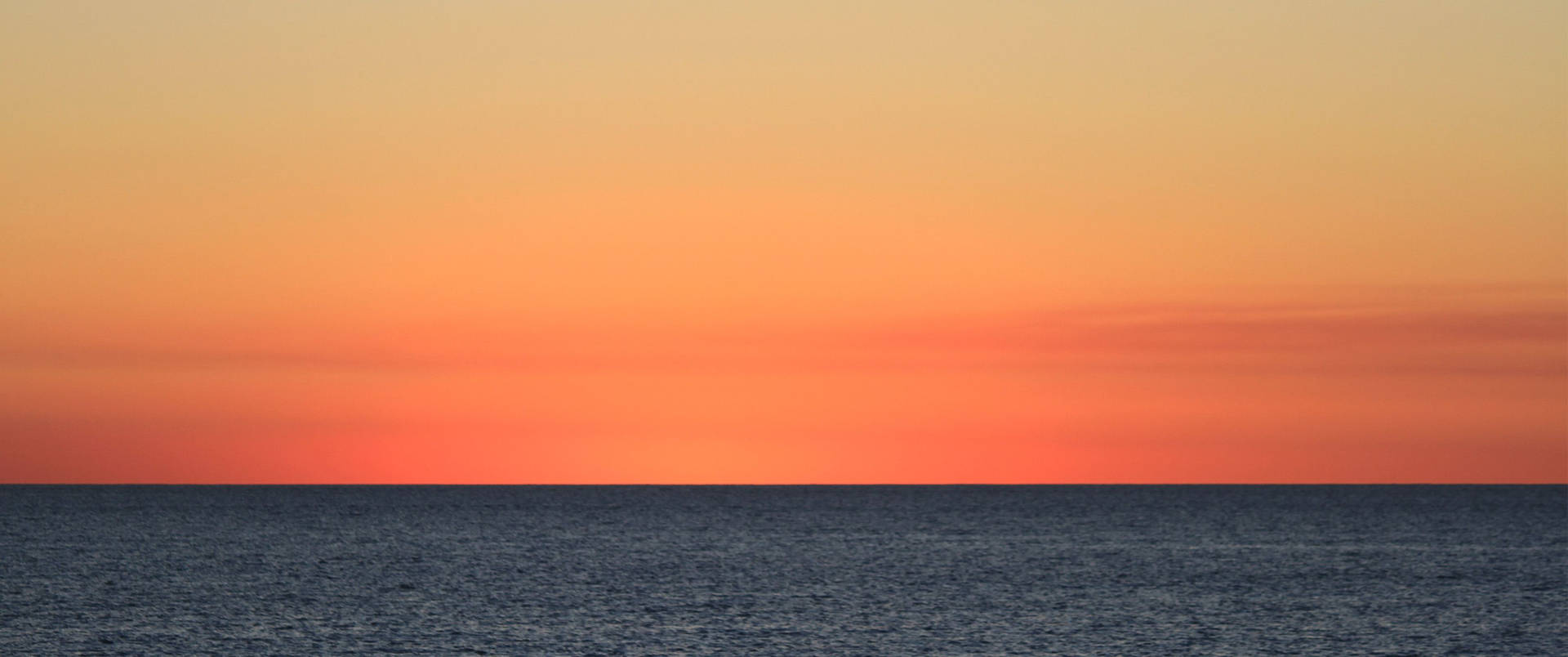 日落時平靜的海洋，天空呈現橙色和藍色漸變 — 3440X1440 壁紙