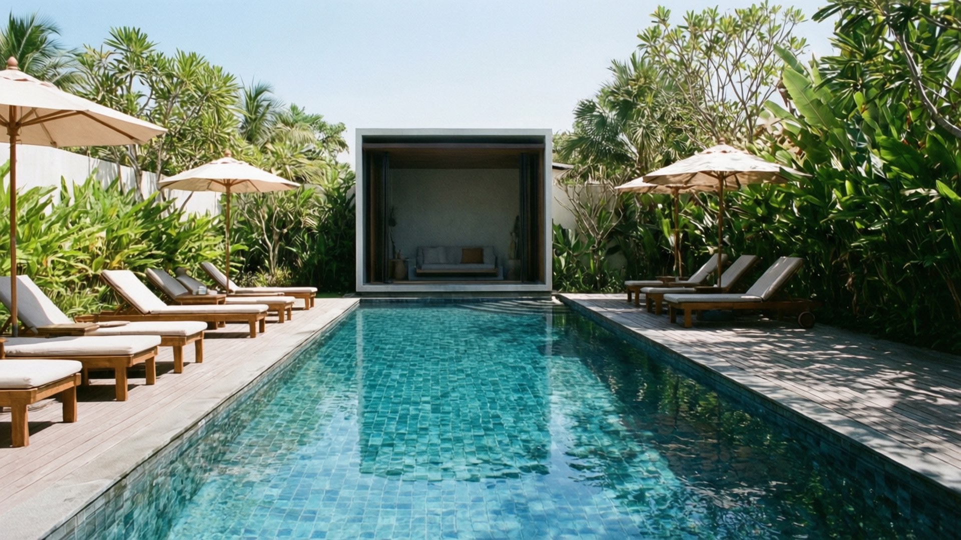 Modern Poolside Retreat 壁紙 — 一個寧靜的熱帶泳池，兩旁擺放著木製躺椅和米色遮陽傘，盡頭有茂密的綠植和現代涼亭。
