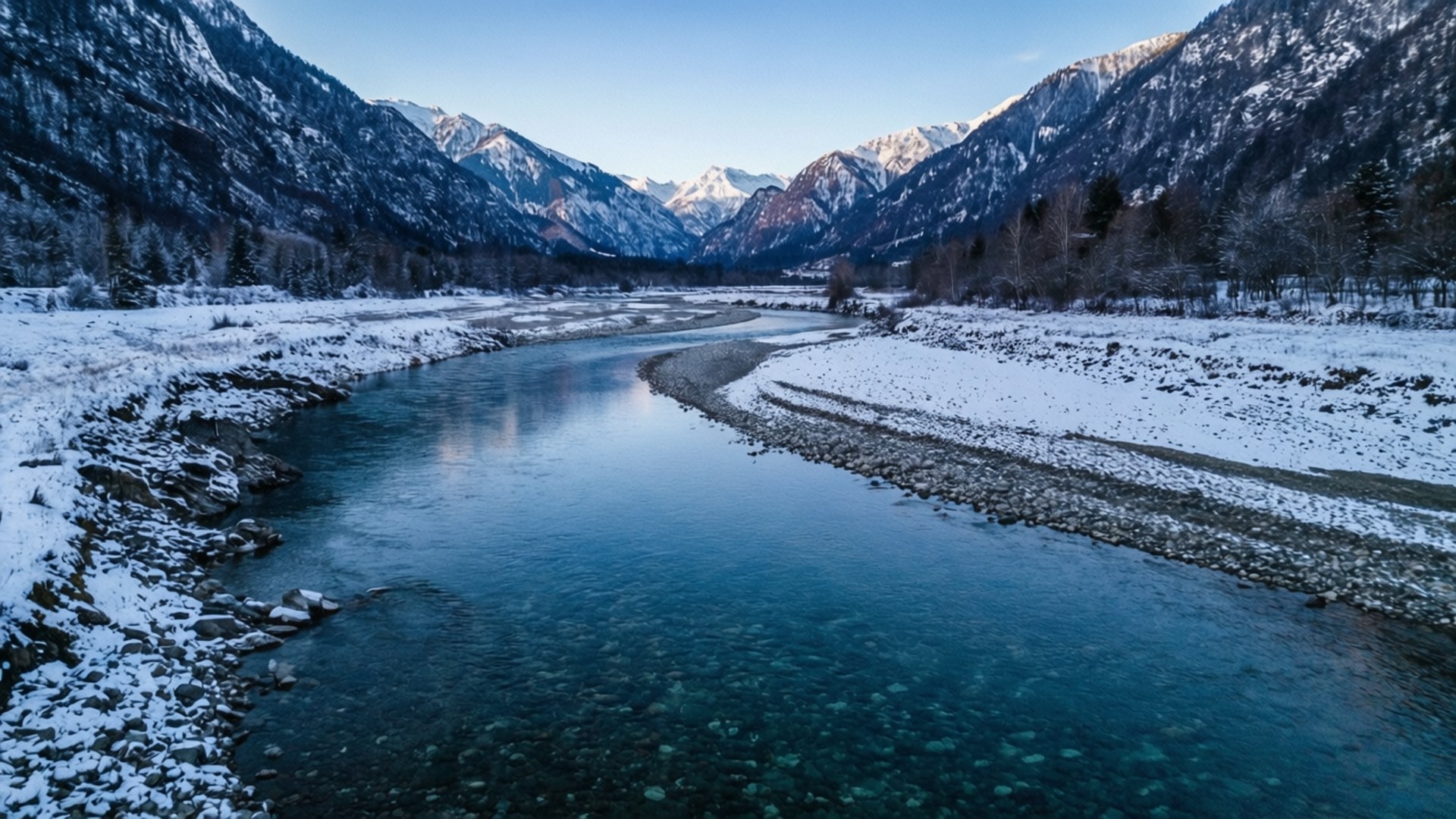River Through Snow 壁紙 — 一條寧靜的冬季河流蜿蜒穿過白雪覆蓋的山脈，在清澈的藍天下。