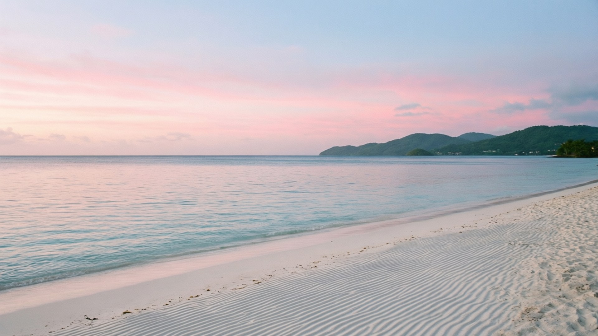 Pastel Morning Calm 壁紙 — 黎明時分寧靜的海灘，粉紅色的天空，藍綠色的海水，白沙上的漣漪通向遠處的綠色山丘。