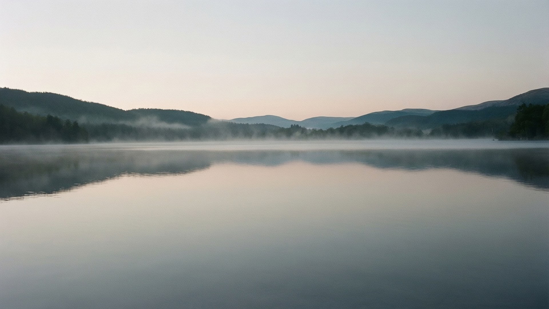Grey Lake Dawn 壁紙 — 黎明時分寧靜的霧湖，平靜的水面映照著柔和的粉彩天空和遠處的森林山丘。