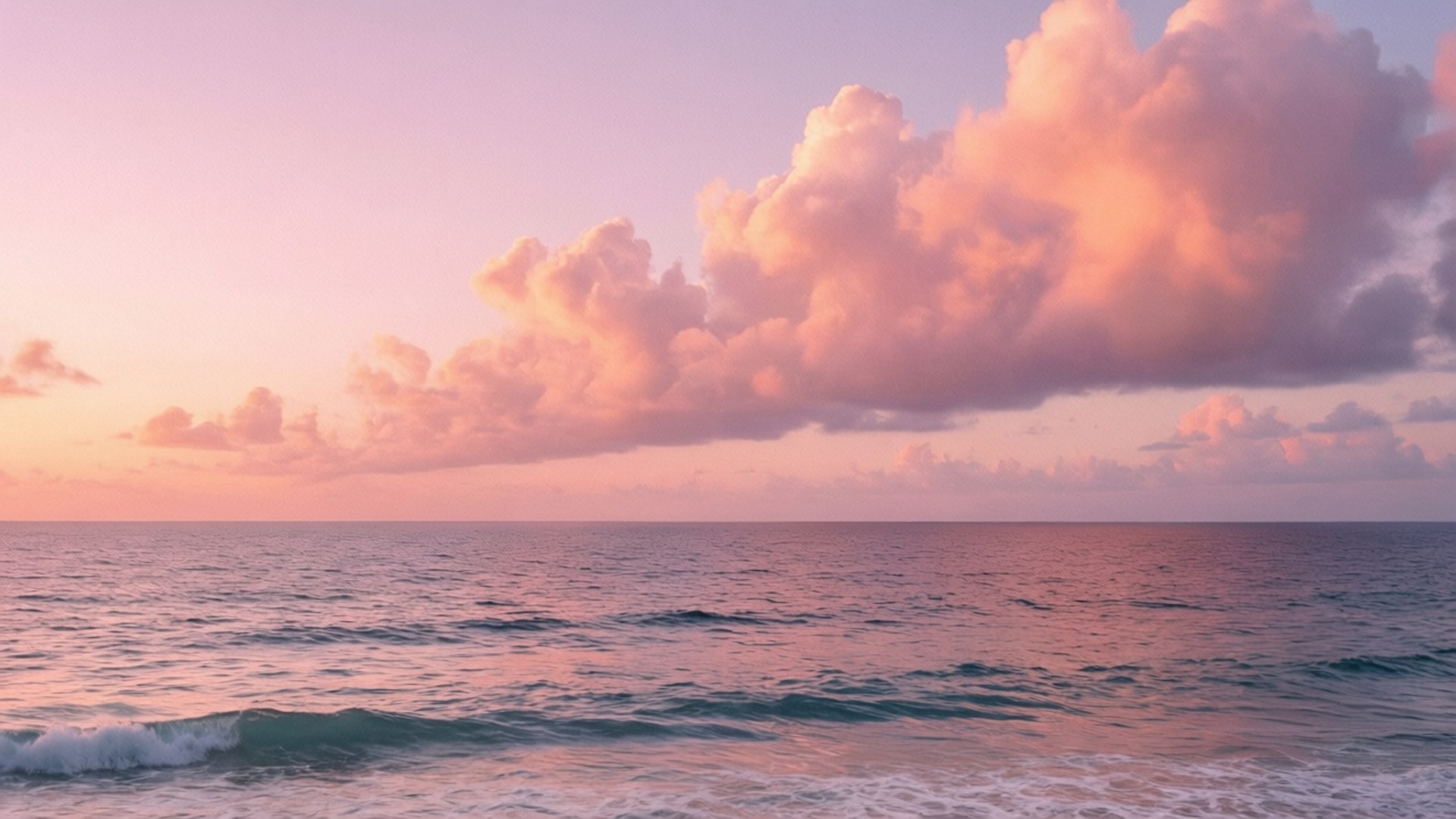 Pastel Ocean Sunset 壁紙 — 寧靜的海洋在日落時分，柔和的粉紅雲朵倒映在平靜的水面上，溫柔的波浪緩緩湧入。