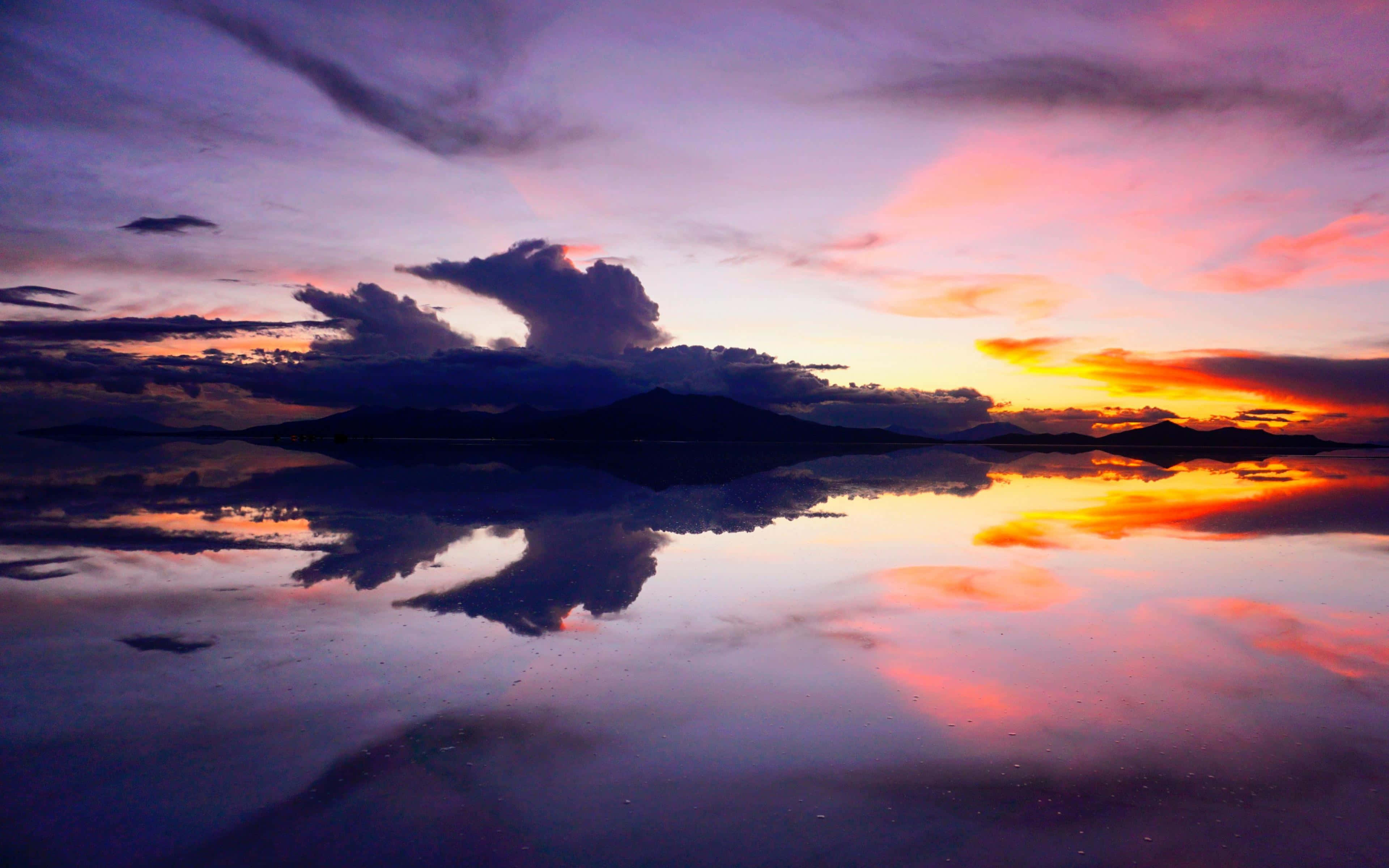 Sunset Reflection 桌布 壁紙 — 平靜湖面上的寧靜日落，映照出火紅的橙色和紫色雲彩，襯托著黑暗的山巒剪影。