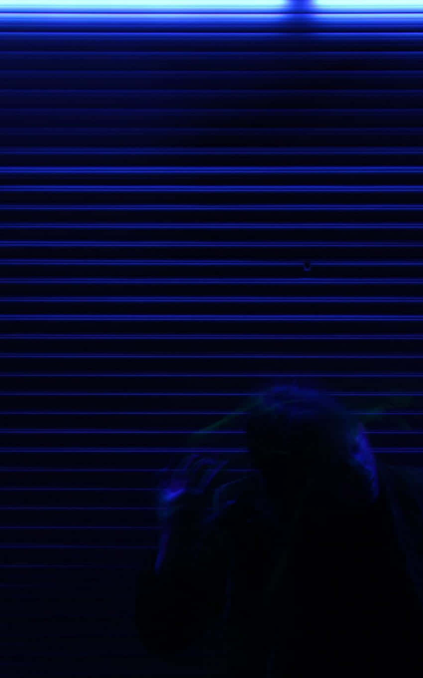  壁紙 — 一個陰暗的身影坐在透過水平百葉窗投射的深藍色霓虹燈光中，營造出憂鬱的城市剪影。