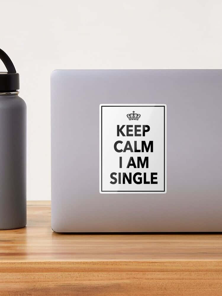  壁紙 — 一台銀色筆記型電腦貼有「Keep Calm I Am Single」貼紙，旁邊有一個灰色水瓶，放在木桌上。