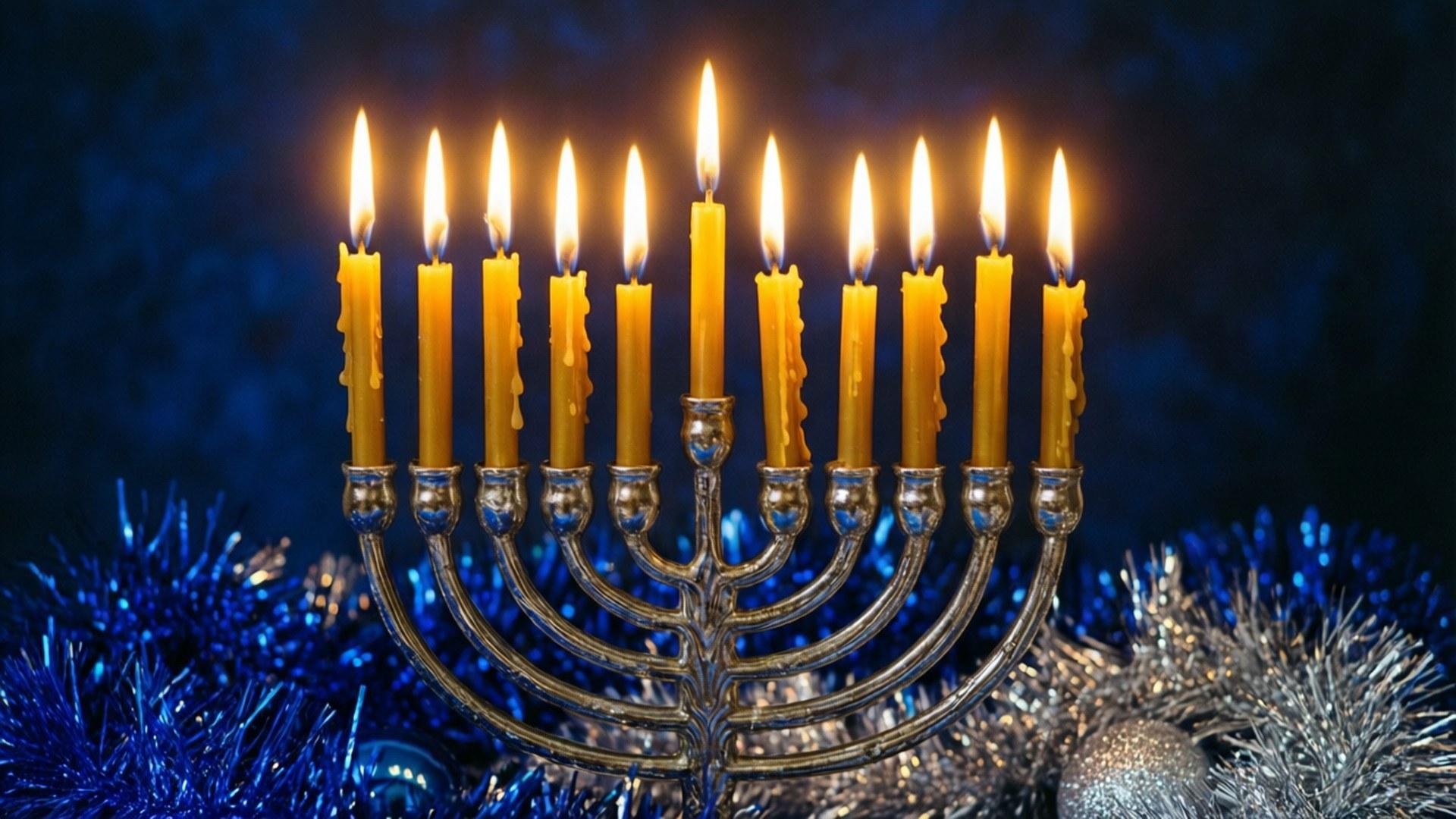 Hanukkah Menorah Glow 壁紙 — 一個銀色燭台上有九支點燃的黃色蠟燭，在深藍色背景上溫暖地發光，背景裝飾著藍色和銀色的閃粉。