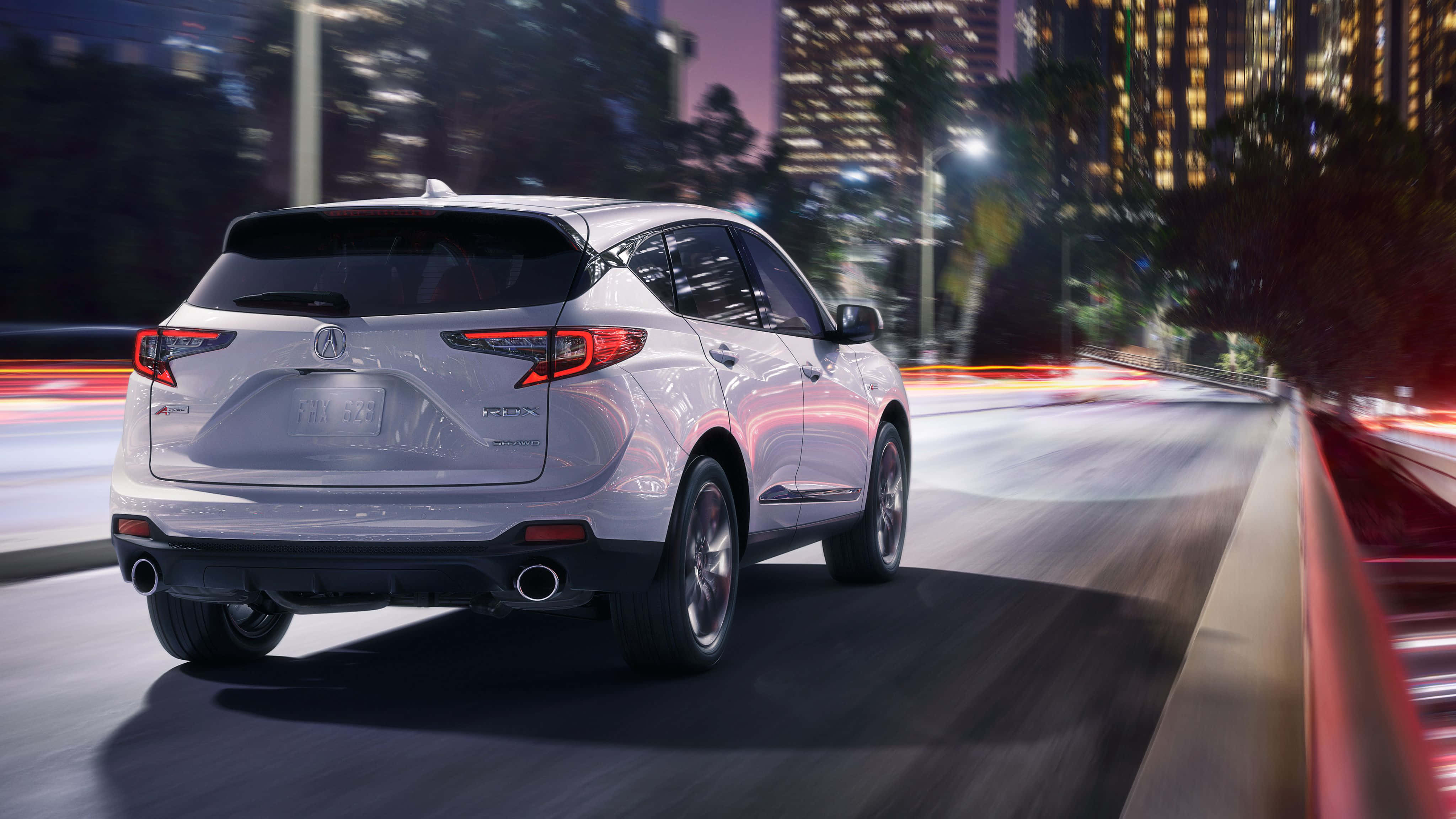 Acura Rdx 桌布 壁紙 — 一輛銀色SUV在夜間疾馳穿過充滿活力的城市，背景中燈光流動，高樓大廈閃爍發光。