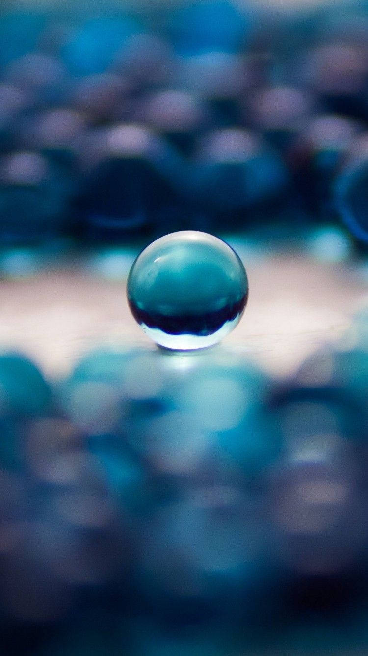 一顆帶有藍色反射的玻璃彈珠位於模糊的藍色彈珠之間。 — iPhone X 壁紙