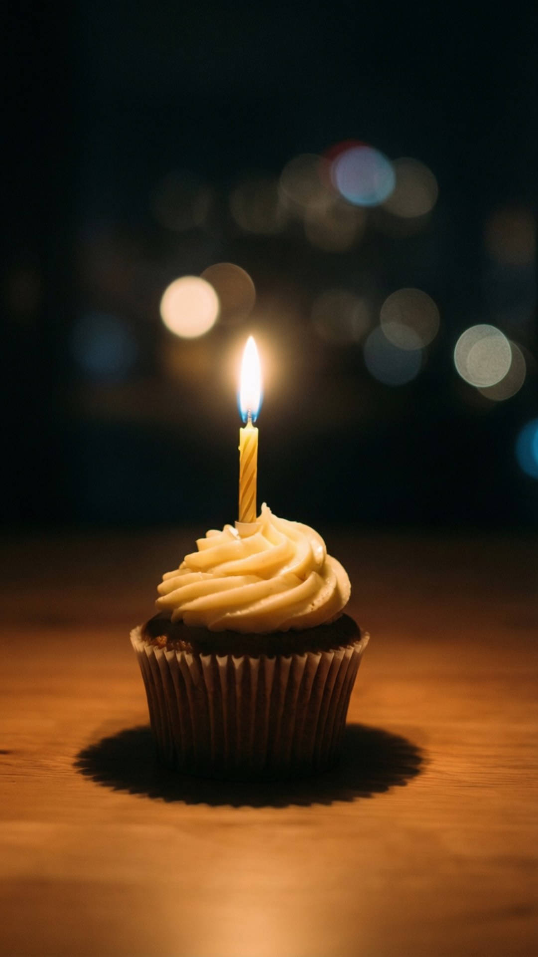 Single Candle Cupcake 壁紙 — 一個巧克力紙杯蛋糕上插著一支點燃的蠟燭，奶油糖霜在黑暗的散景背景下溫暖地發光。