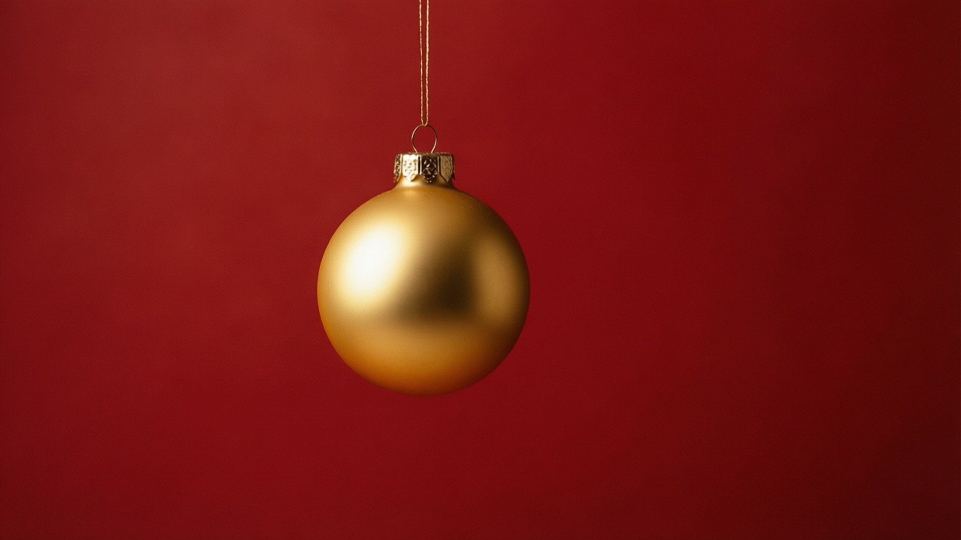 Single Gold Ornament 壁紙 — 一個啞光金色聖誕裝飾品用細繩掛在純深紅色背景上。