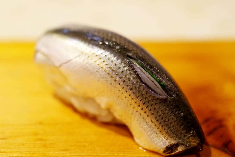  壁紙 — 一件新鮮壽司上面放著一整條魚，擱在溫暖的木板上。