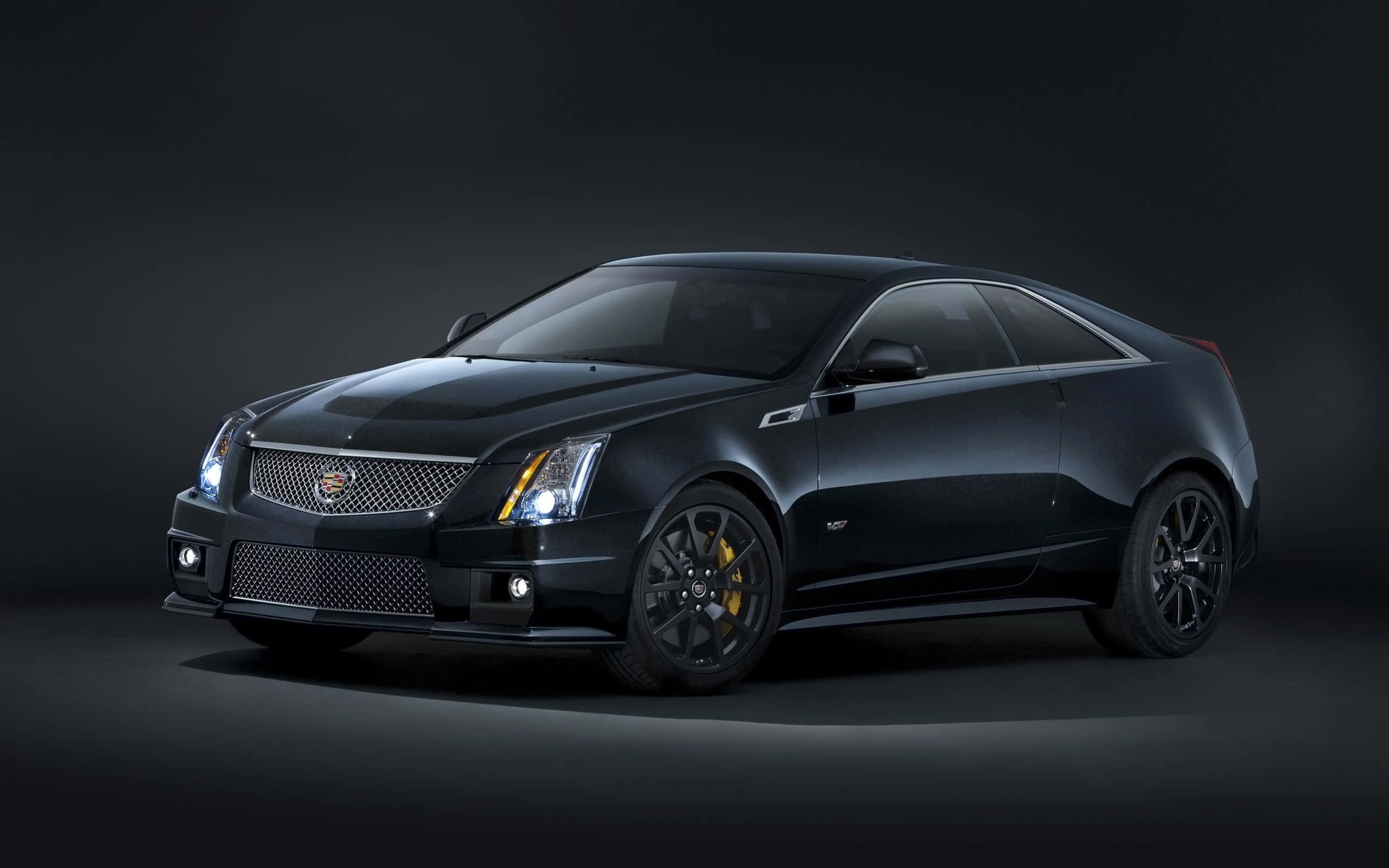 Cadillac Cts 桌布 壁紙 — 一輛時尚的黑色 Cadillac CTS-V 雙門轎跑車，帶有發光的頭燈和黃色制動卡鉗，在黑暗的攝影棚背景下擺拍。