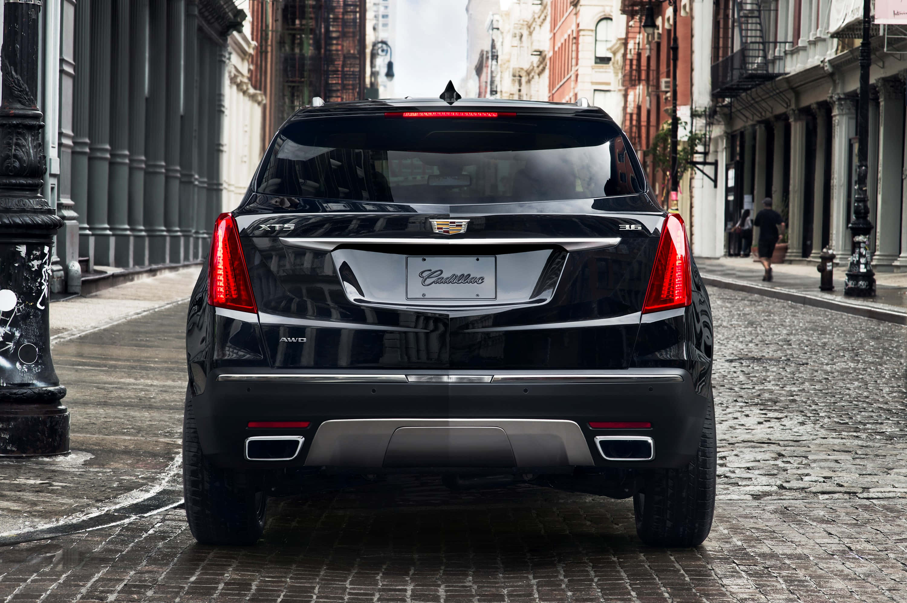 Cadillac Xt5 桌布 壁紙 — 一輛時尚的黑色凱迪拉克SUV停在濕漉漉的鵝卵石街道上，兩旁是歷史悠久的磚造建築。