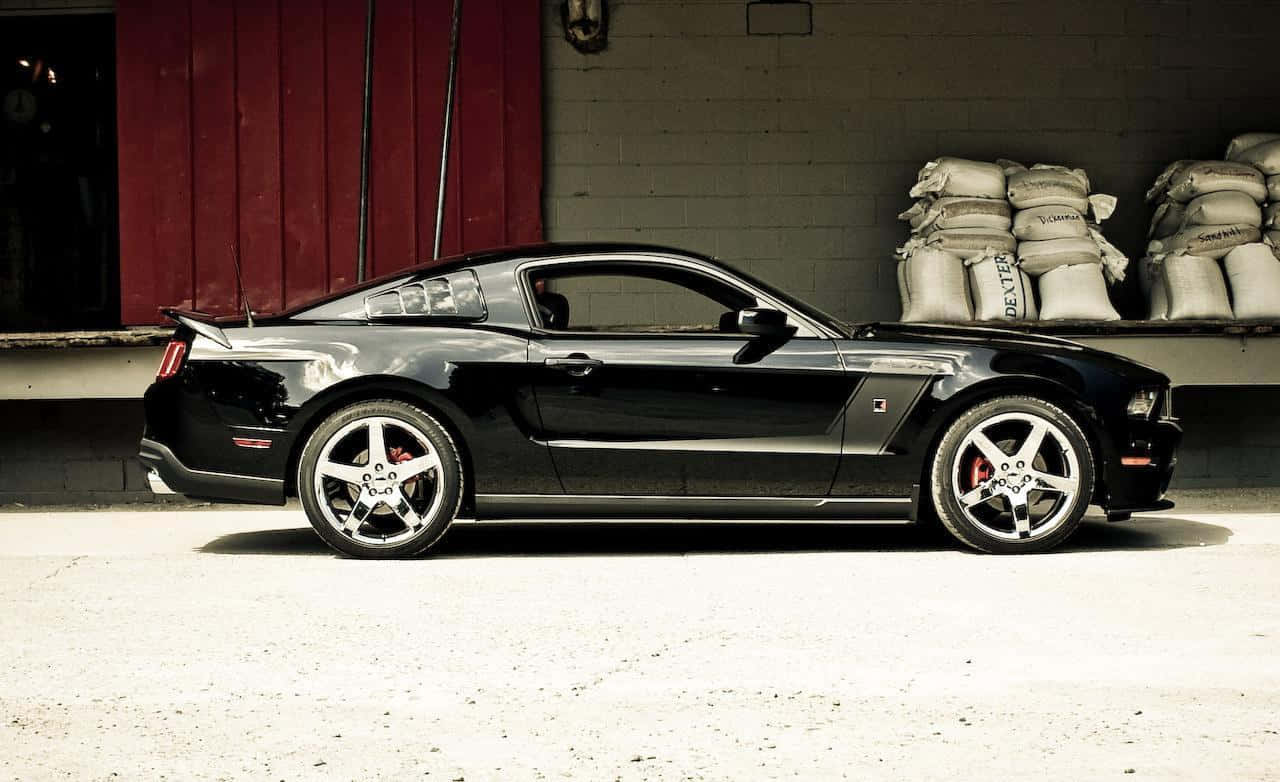 Ford Mustang Roush 桌布 壁紙 — 一架時尚的黑色福特Mustang跑車停在紅色穀倉前，附近有麻袋堆疊。