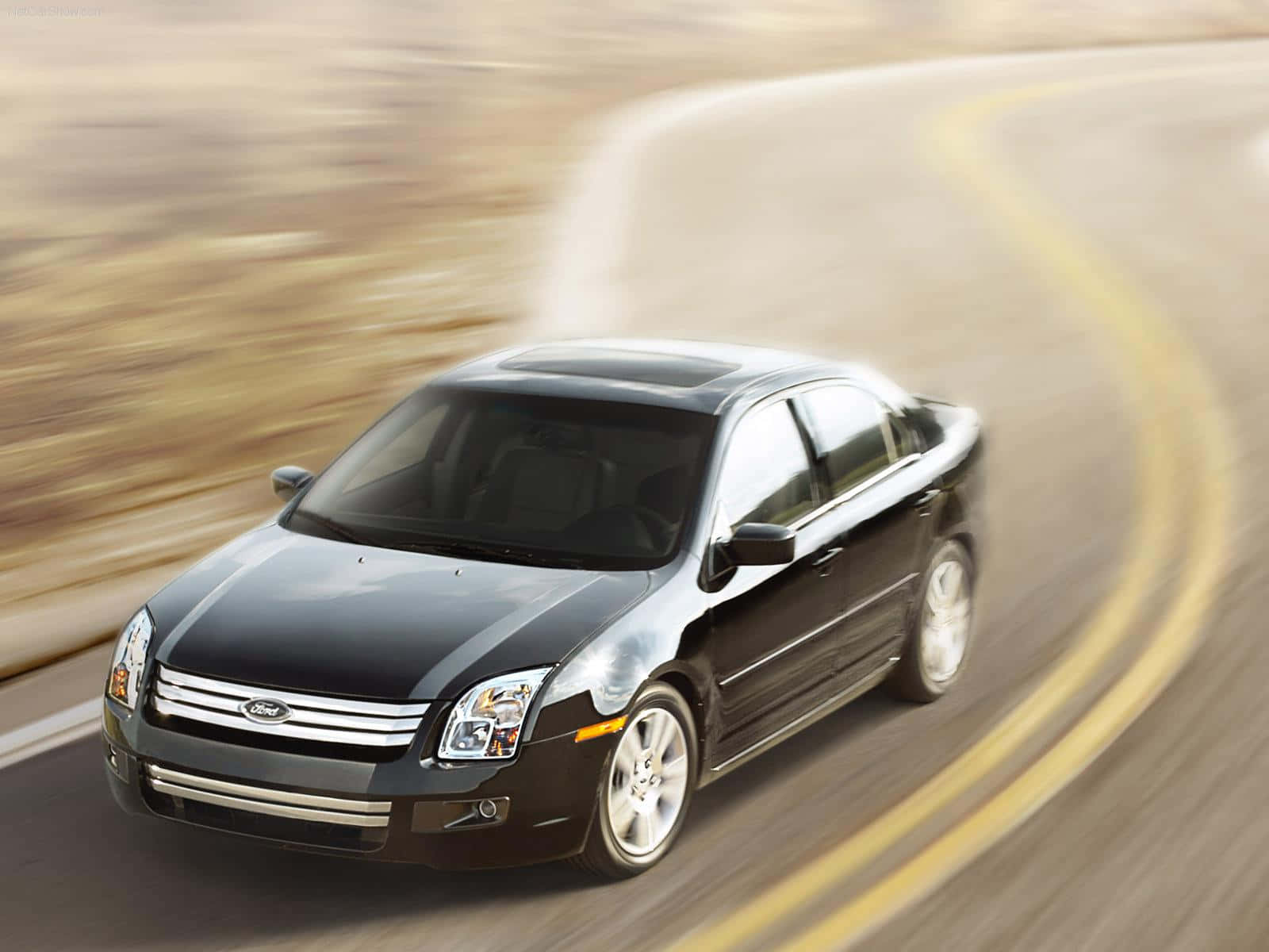 Ford Fusion 桌布 壁紙 — 一輛時尚的黑色福特轎車沿著彎曲的道路疾馳，動態模糊強調了其動態運動。