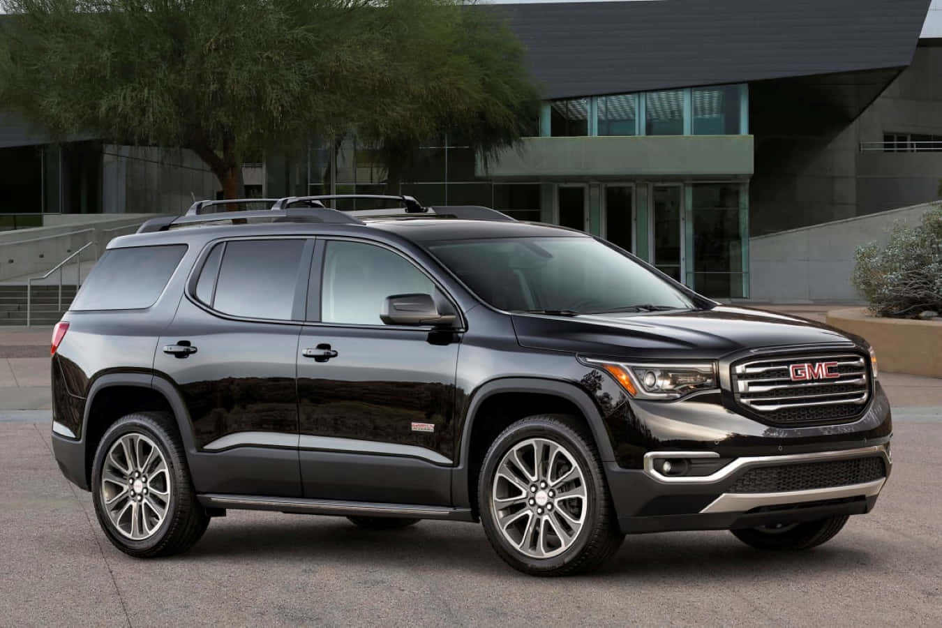 Gmc Acadia 桌布 壁紙 — 一輛時尚的黑色GMC Acadia SUV停在一棟現代玻璃建築前，附近有樹木。