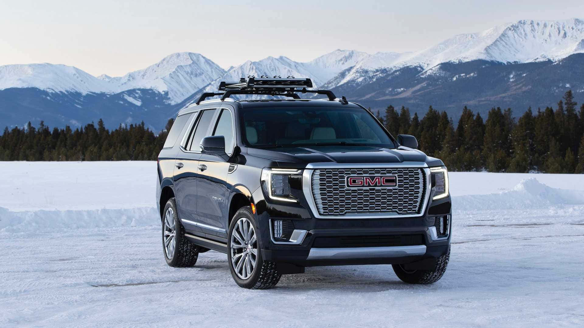 Gmc Yukon 桌布 壁紙 — 一輛時尚的黑色GMC Yukon停在冰凍的湖面上，背景是白雪覆蓋的山脈和常青樹。