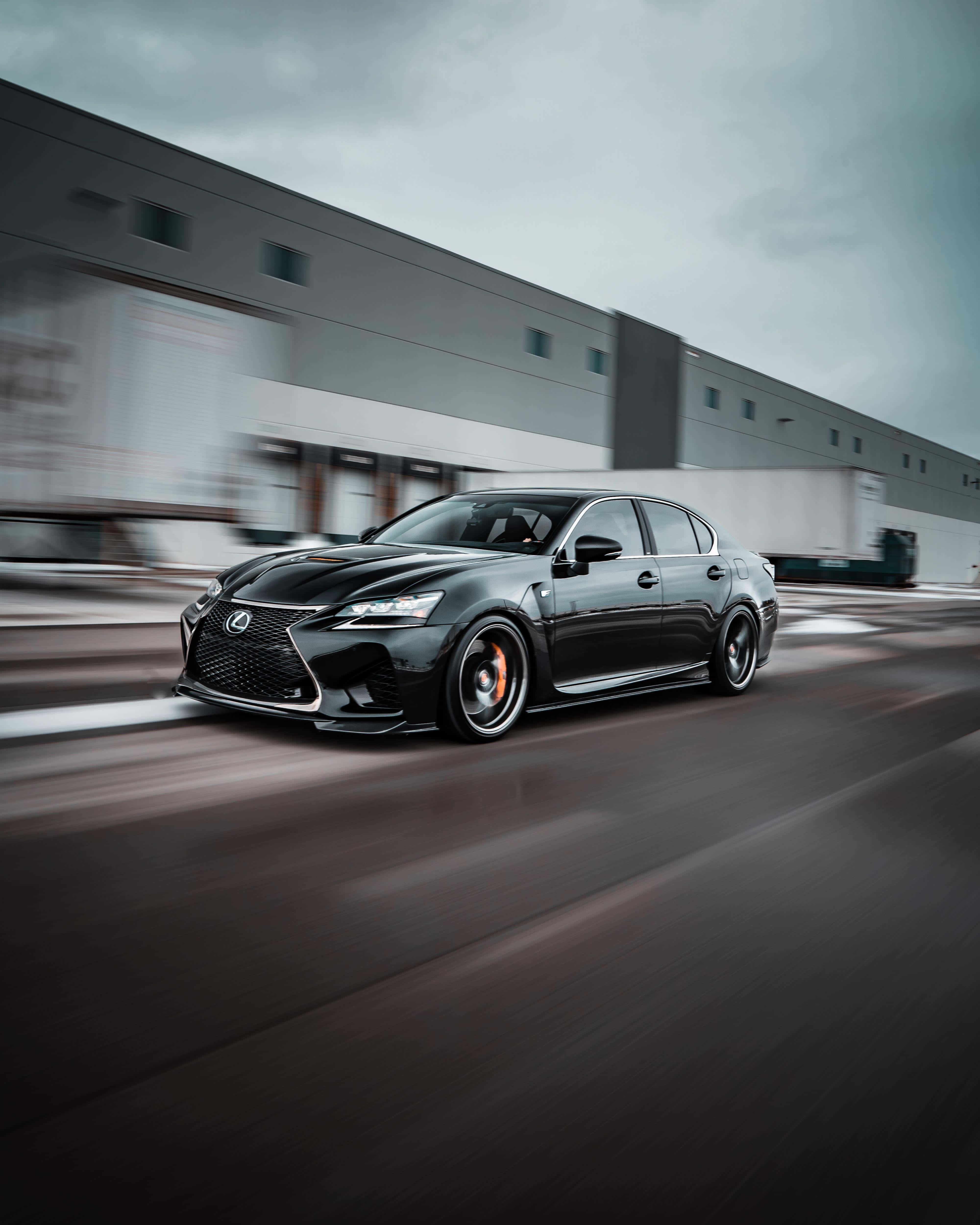 Lexus Gs F 桌布 壁紙 — 一輛時尚的黑色凌志房車高速駛過倉庫，動態模糊強調其動感移動。