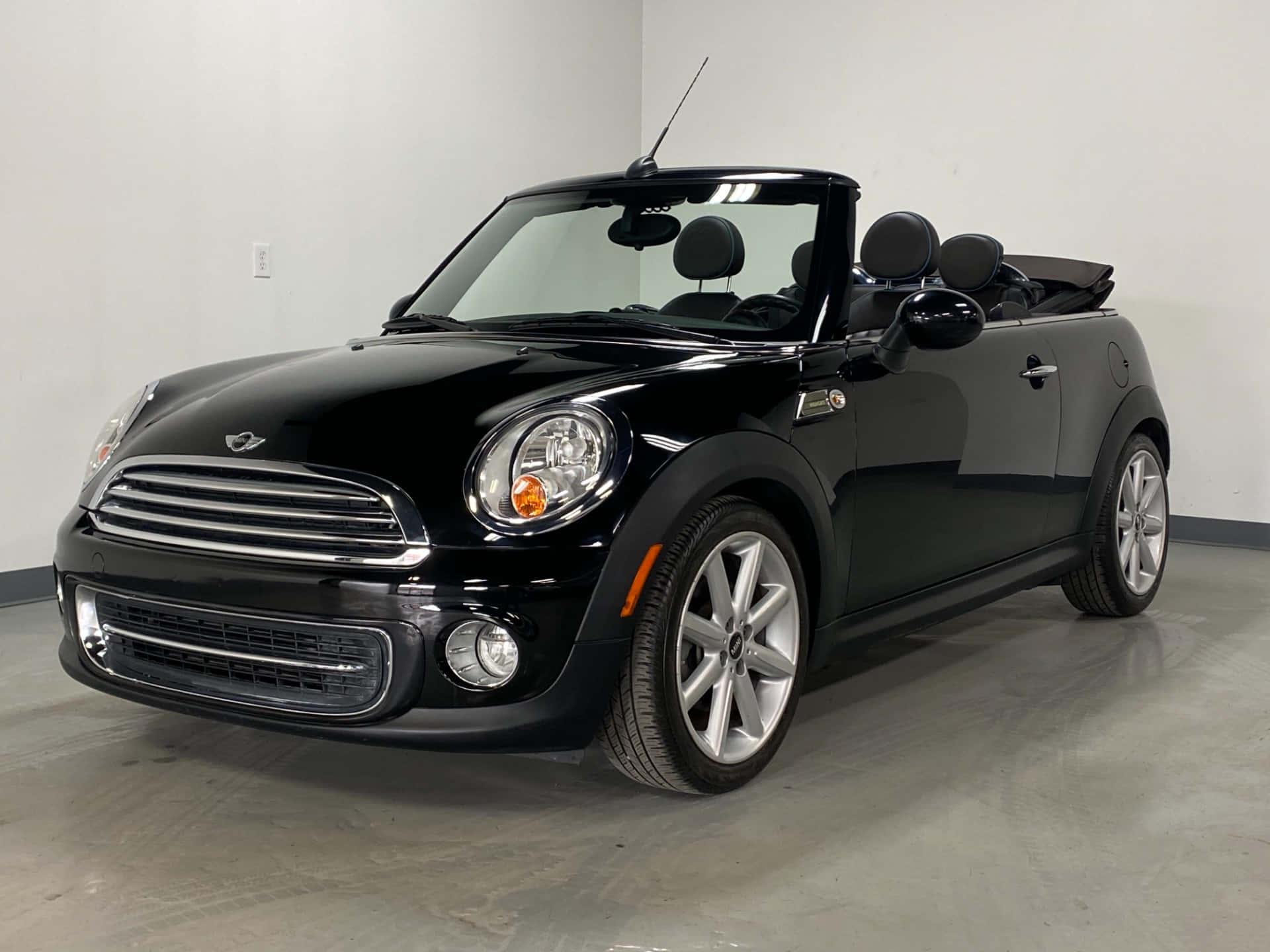 Mini Cooper Convertible 桌布 壁紙 — 一輛時尚的黑色MINI Cooper敞篷車停放在室內，車頂敞開，展示閃亮的鍍鉻飾件和銀色輪圈。