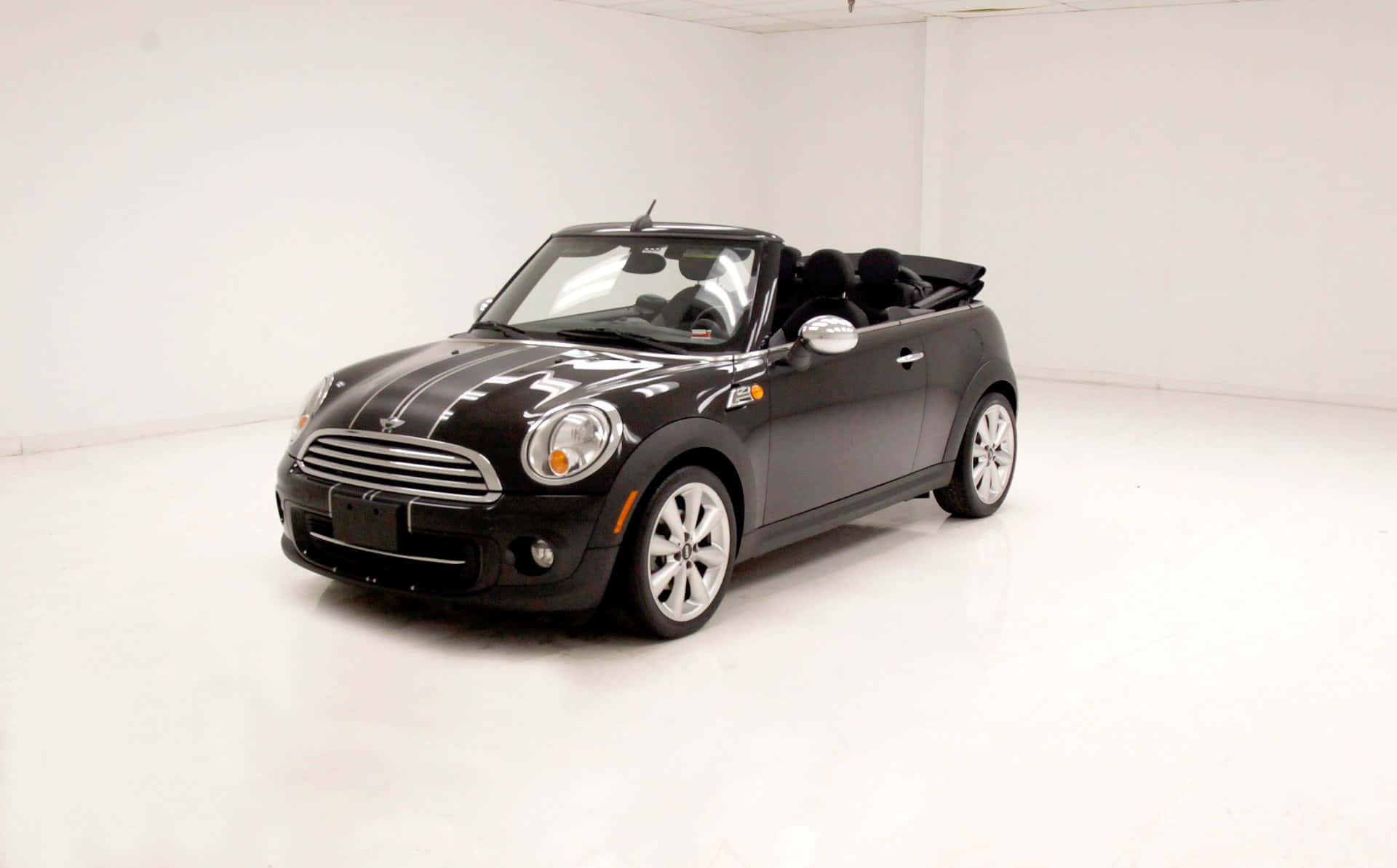 Mini Cooper Convertible 桌布 壁紙 — 一輛時尚的黑色Mini Cooper敞篷車，帶有白色賽車條紋，停在明亮的白色攝影棚空間中。