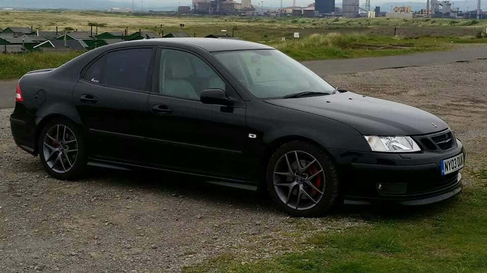 Saab 99 桌布 壁紙 — 一輛時尚的黑色Saab 9-3運動轎車停在碎石路上，遠方朦朧可見工業建築。