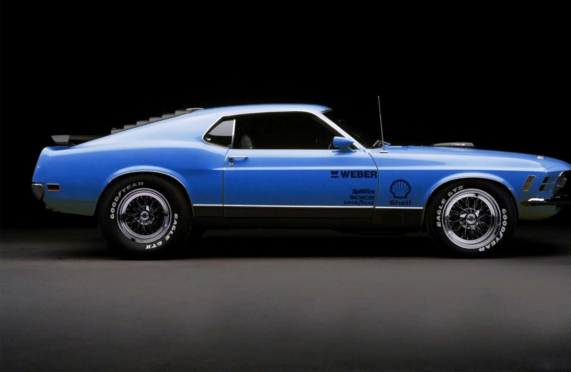 Ford Mustang Mach 1 桌布 壁紙 — 一輛時尚的藍色經典肌肉車帶有賽車貼花，在昏暗的攝影棚環境中展示。