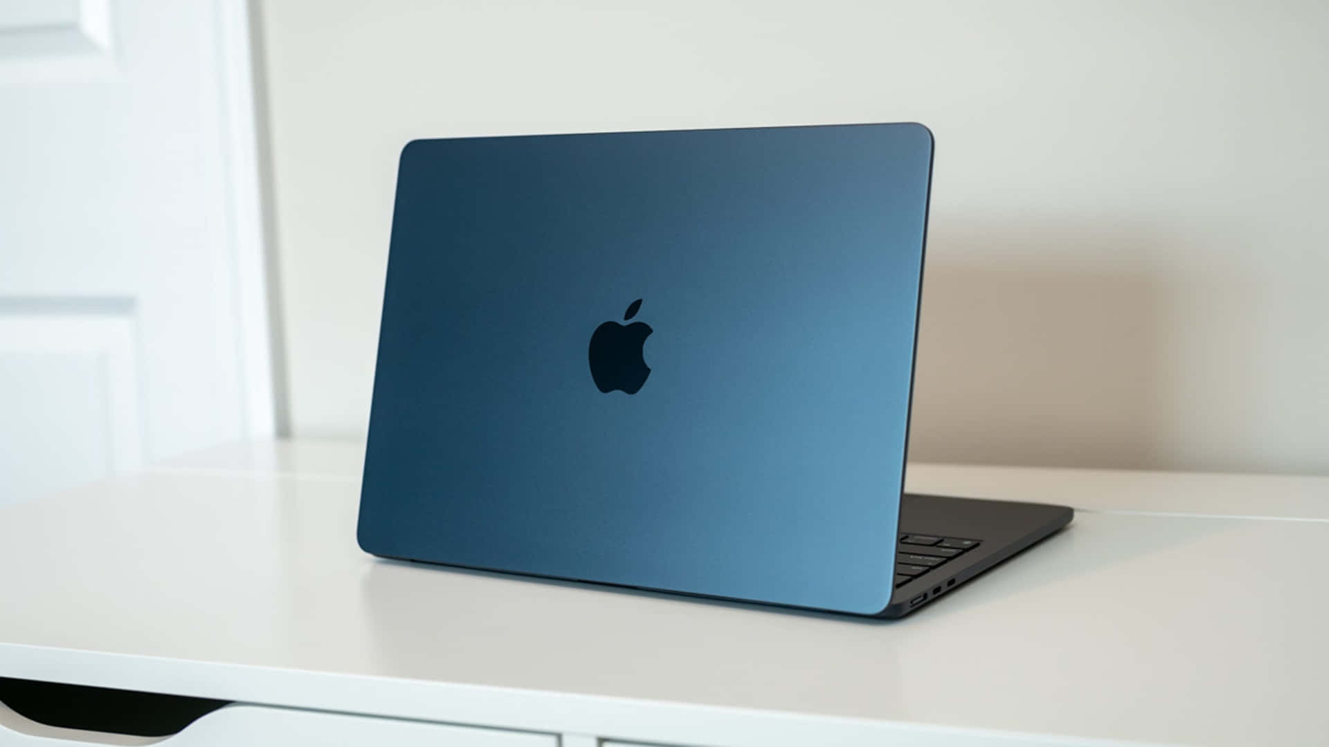 藍色 MacBook 筆記型電腦在明亮的房間中打開放在白色桌子上。 — Macbook Pro 壁紙