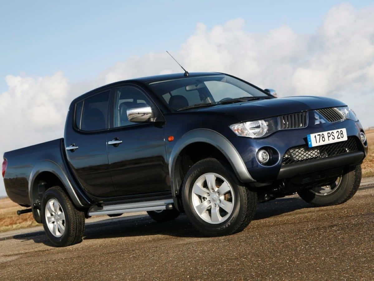 Mitsubishi L200 桌布 壁紙 — 一輛時尚的深藍色三菱L200皮卡車停在碎石路上，天空部分多雲。