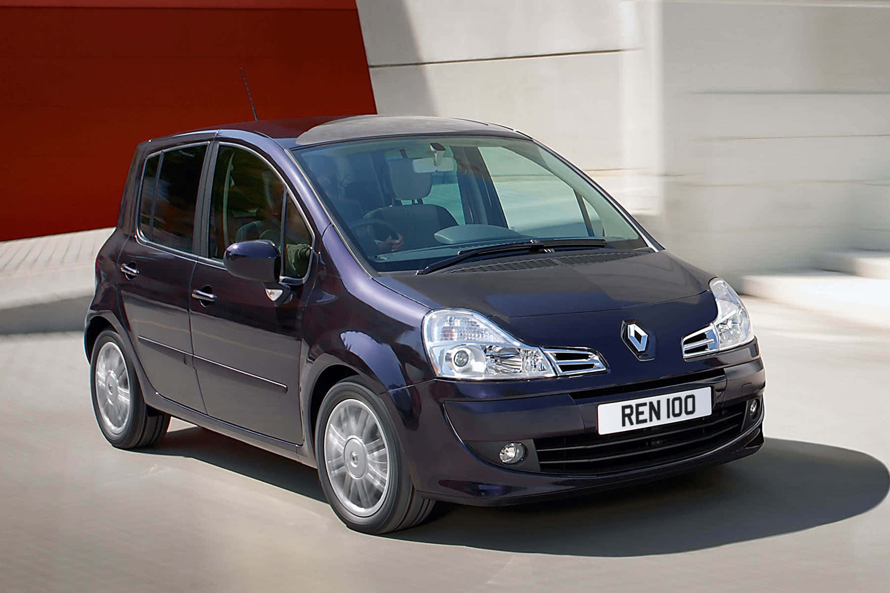 Renault Modus 桌布 壁紙 — 時尚深藍色雷諾100掀背車在現代紅米色建築背景下向前滑行。