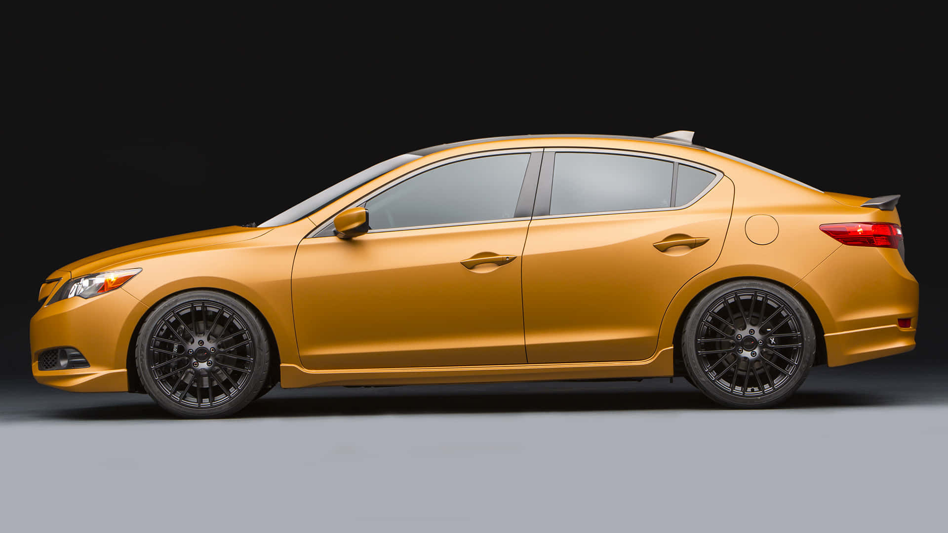 Acura Ilx 桌布 壁紙 — 一輛時尚的黃金轎車搭配黑色輪圈，在黑暗的攝影棚背景下側面展示。
