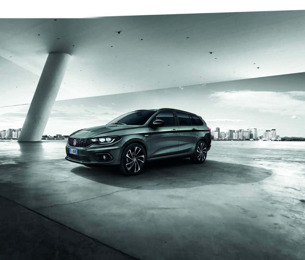 Fiat Tipo 桌布 壁紙 — 一輛時尚的灰色旅行車停放在現代混凝土天橋下，背景是城市天際線。