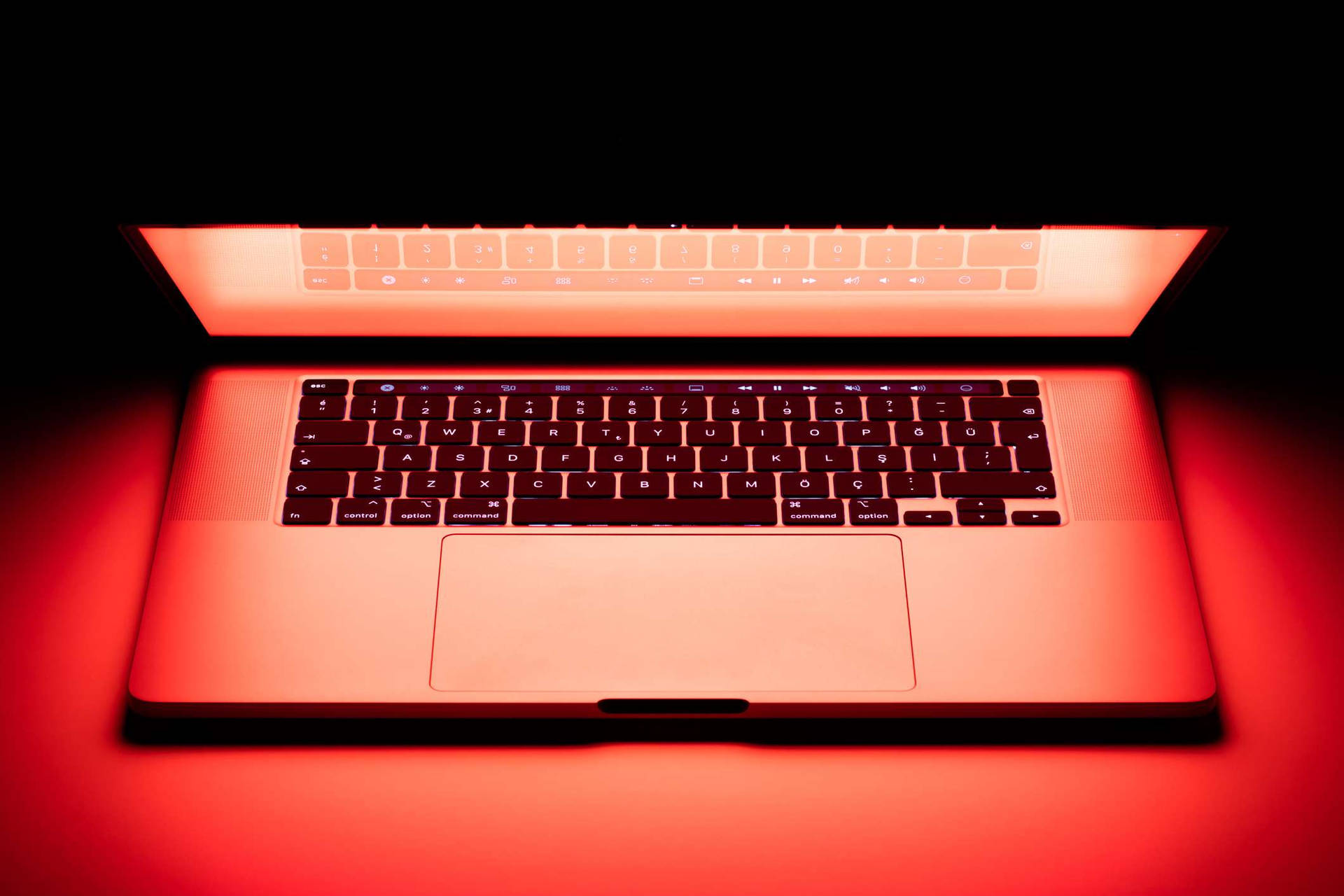 在黑暗表面上帶有環境照明的發光紅色筆記型電腦。 — Macbook Pro 壁紙