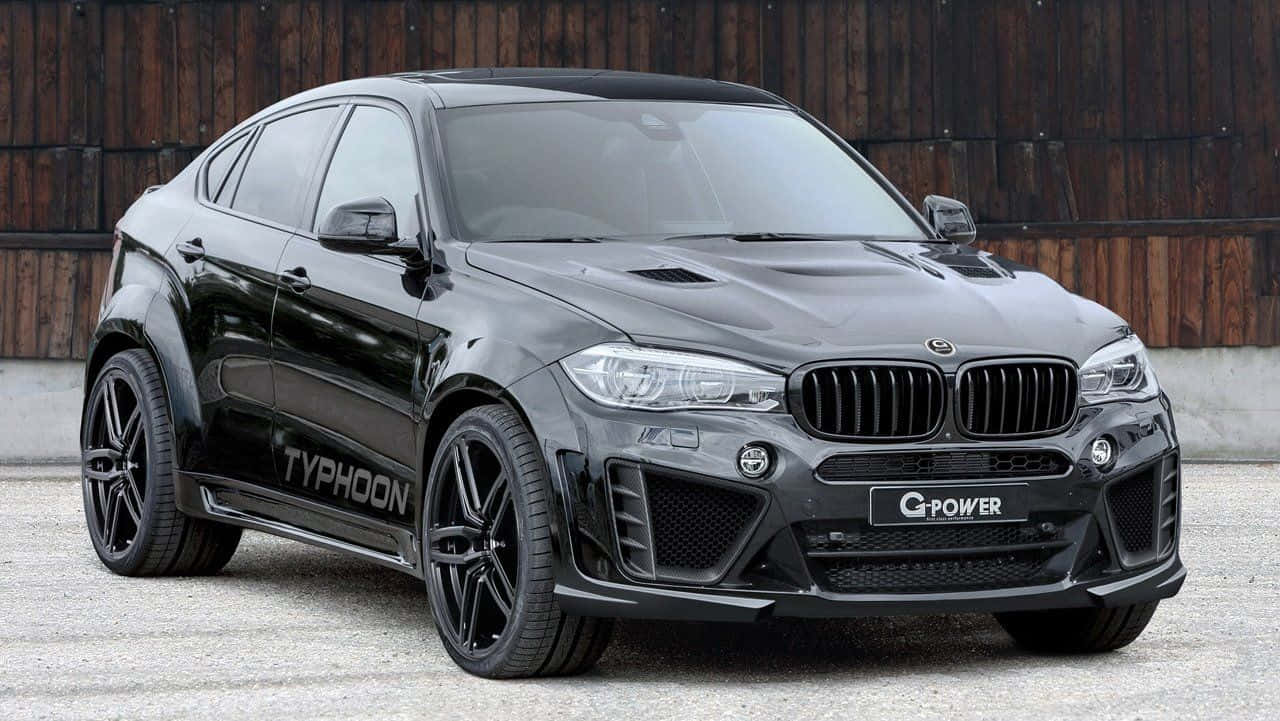 Bmw X6 桌布 壁紙 — 一輛時尚的啞光黑色G-Power Typhoon BMW X6M停放在碎石上，背景是木柵欄。