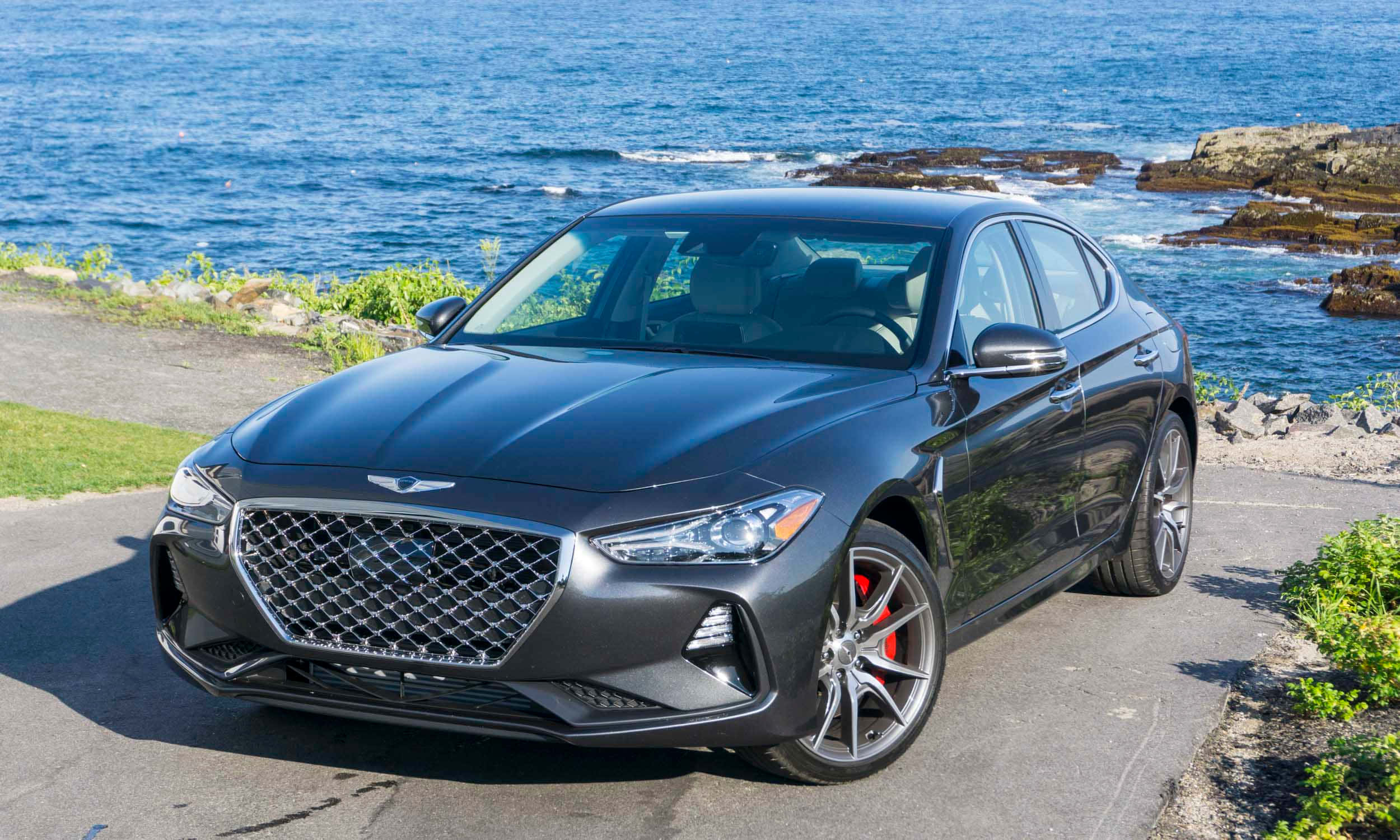 Genesis G70 桌布 壁紙 — 一輛時尚的啞光灰色 Genesis G70 運動轎車停泊在沿海道路上，背景是洶湧的藍色海浪和岩石峭壁。