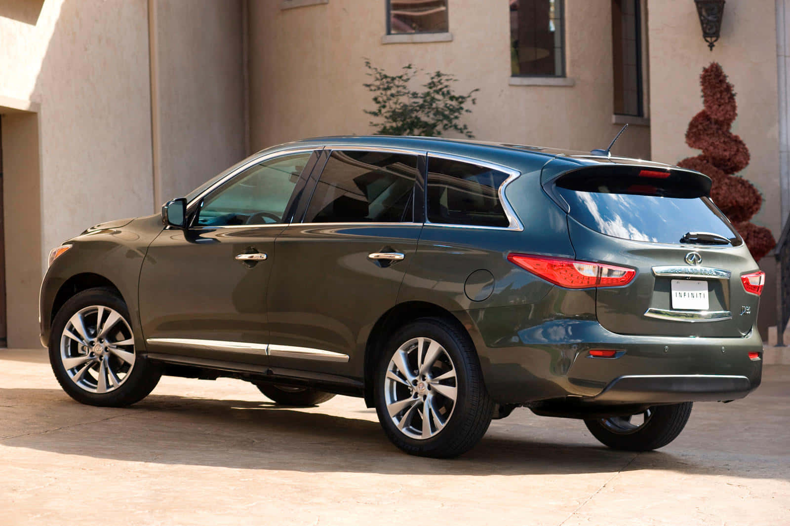 Infiniti Jx35 桌布 壁紙 — 一輛時尚的橄欖綠色 Infiniti QX70 SUV 停在米色灰泥建築前，在明亮的日光下。