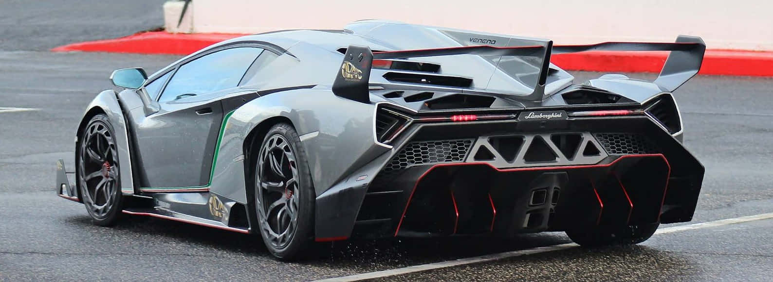 Lamborghini Veneno 桌布 壁紙 — 一架時尚的銀色藍寶堅尼跑車，帶有紅色點綴和大型尾翼，停泊在潮濕的賽道上。