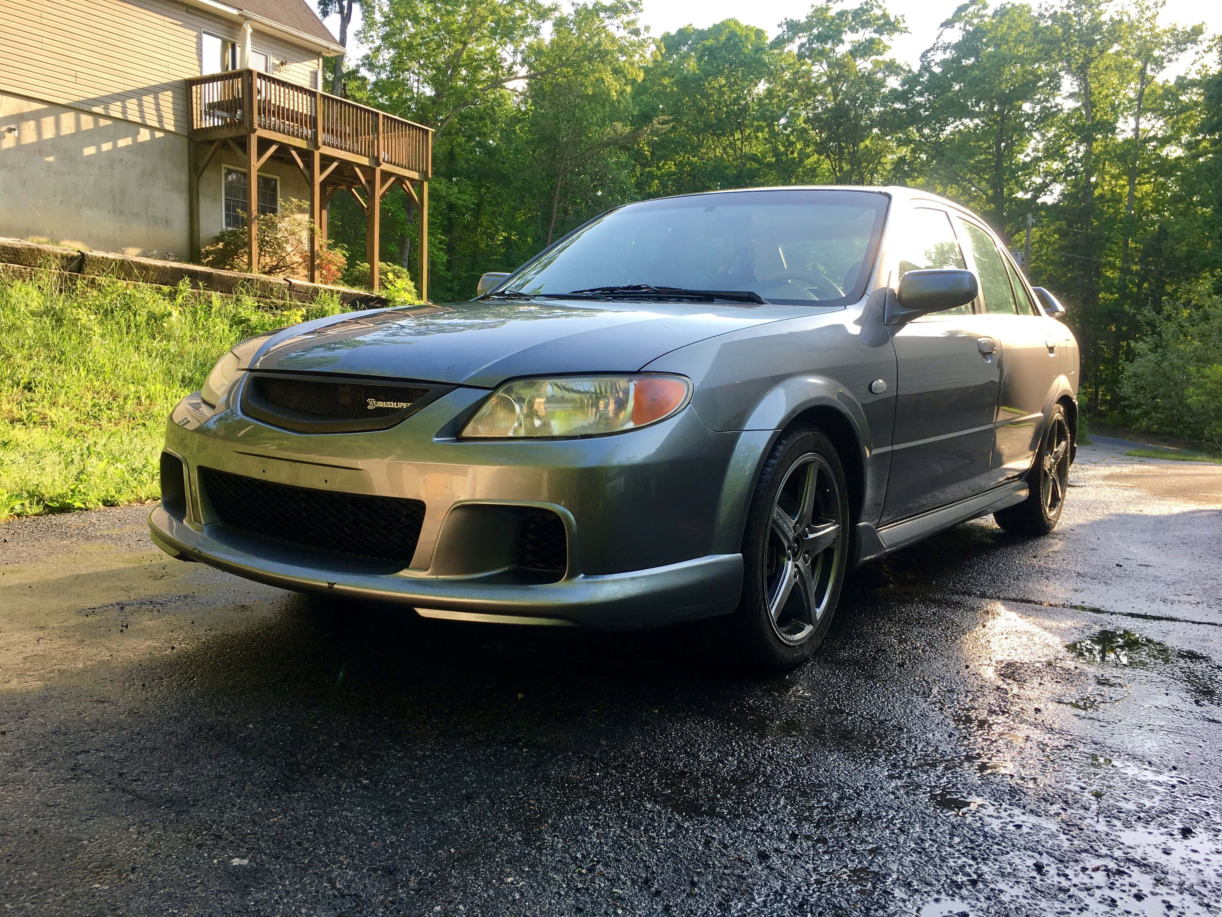 Mazda Protege 桌布 壁紙 — 一輛時尚的銀色馬自達6運動轎車停在濕漉漉的車道上，背景有樹木和房屋。