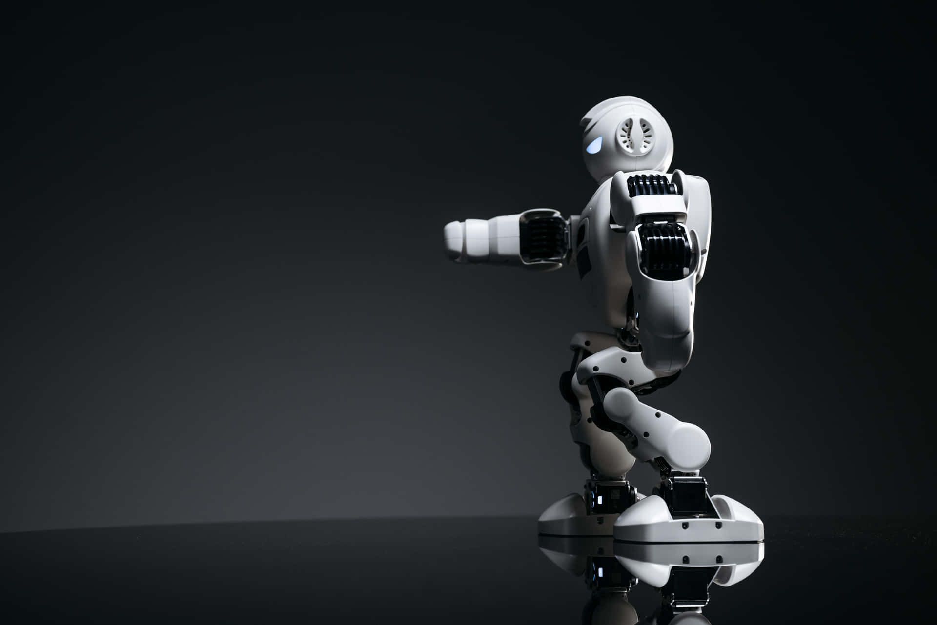 一個白色人形機器人站在黑暗工作室中反光的黑色表面上。 — 3D 壁紙